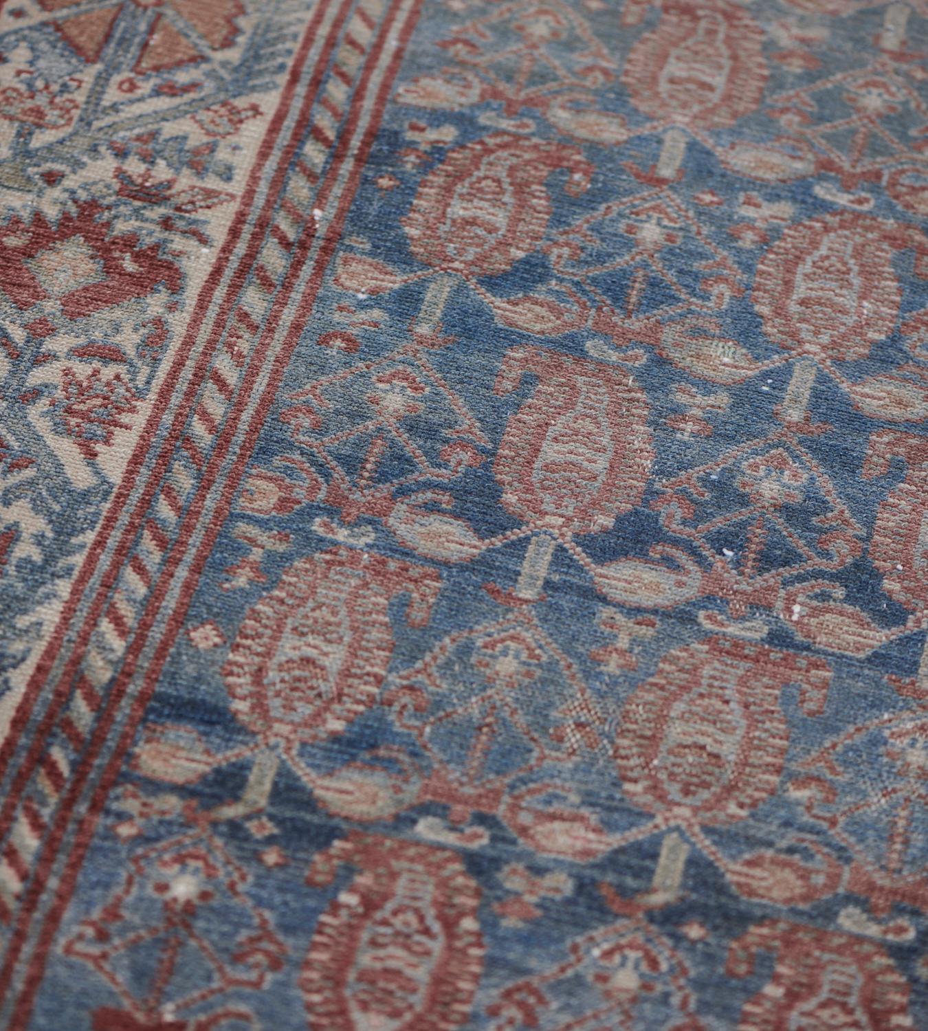 This antique, circa 1910, Malayer runner has a shaded blue field with an overall design of fox-brown boteh linked by an angular floral lozenge and small flowerheads, in a broad ivory border with a dense polychrome angular flowerhead and serrated