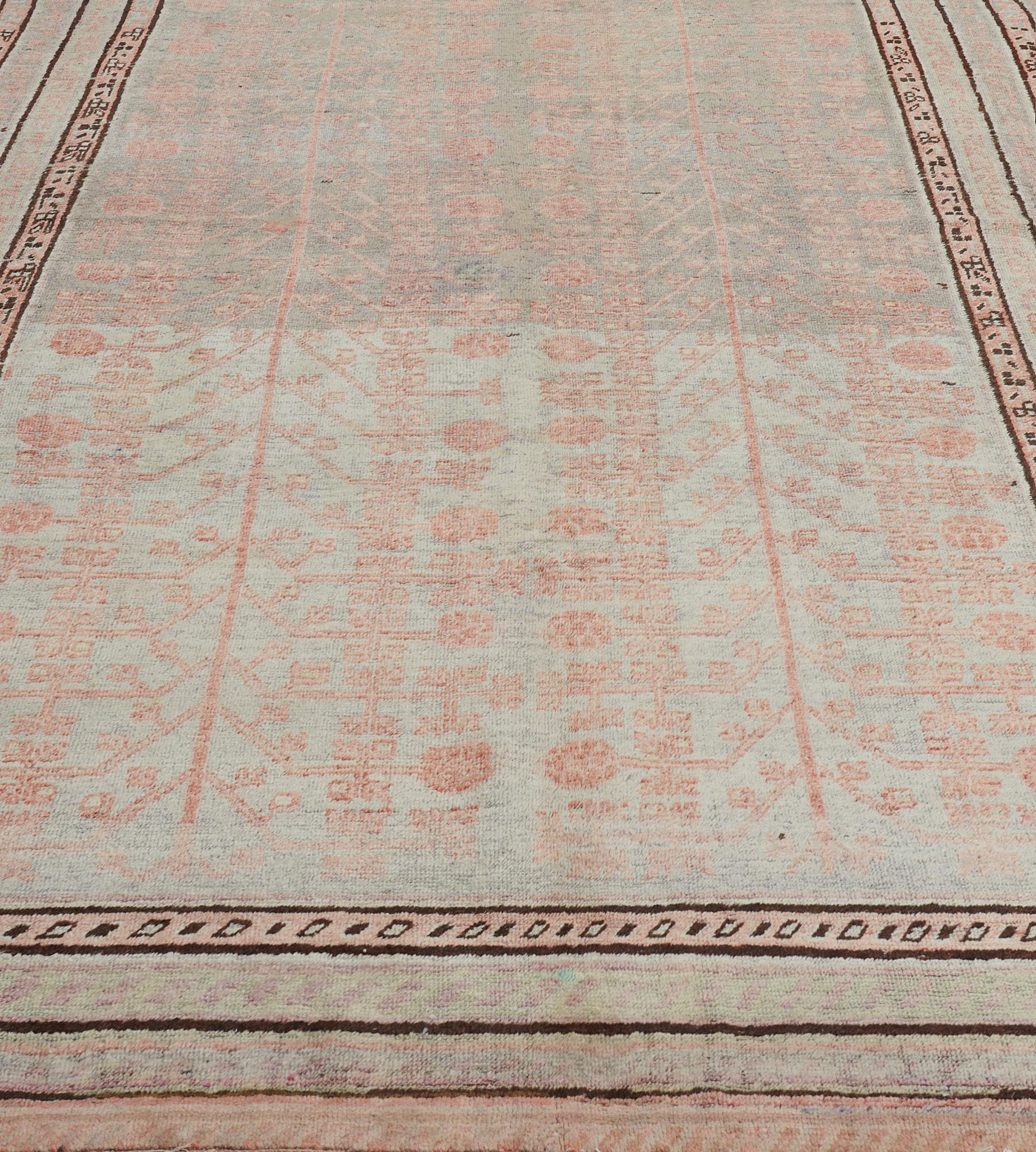 This antique, circa 1920, Khotan rug has a soft shaded grey field with an overall design of soft apricot angular pomegranate vine, in a border of five narrow stripes two with a soft apricot angular lozenge vine and the others with a soft shaded grey