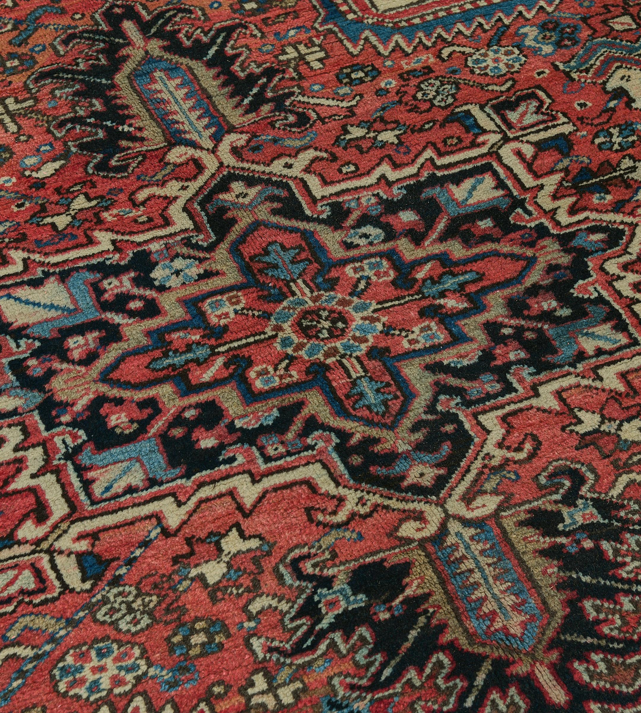 Dieser antike, um 1930 entstandene persische Heriz-Teppich hat ein weiches, tomatenrotes Feld mit einer eckigen, polychromen Blumen- und Blattranke um ein zentrales, kohlschwarzes Rautenmedaillon mit Palmettenanhängern, das ein zentrales,