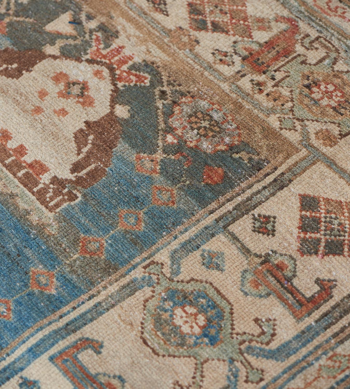 This antique, circa 1940, Malayer rug has a shaded blue field with two vases below and two above issuing stylized floral arrangements which join in the centre, flanked by perching birds, flowerheads and floral stems, in broad ivory border of