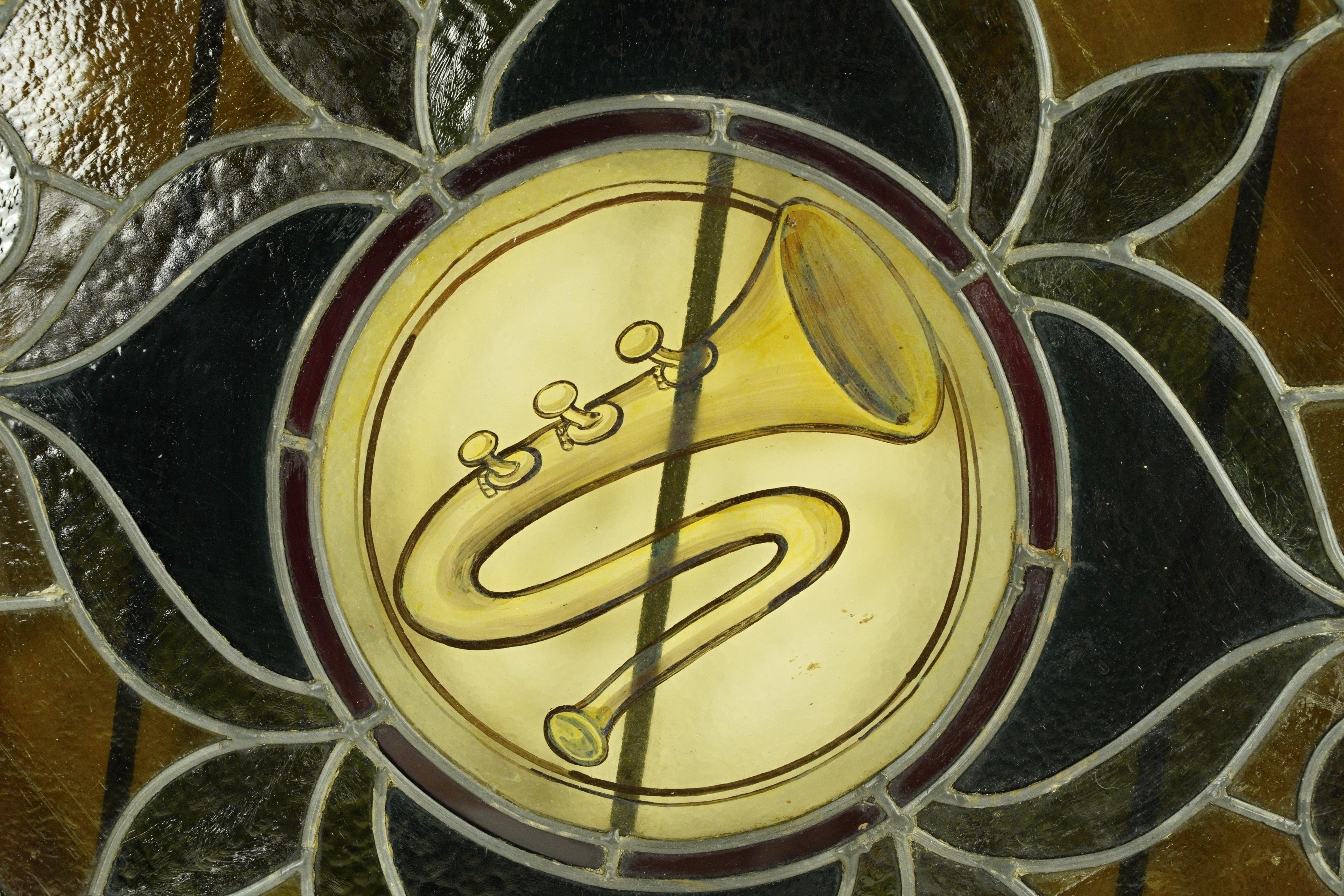 Vitrail ancien de forme circulaire à ouverture battante avec un cadre en pin et une quincaillerie en acier. Elle présente un motif en forme de corne et un verre texturé à motif floral quadruple, dans une palette de couleurs sombres. Bon état avec