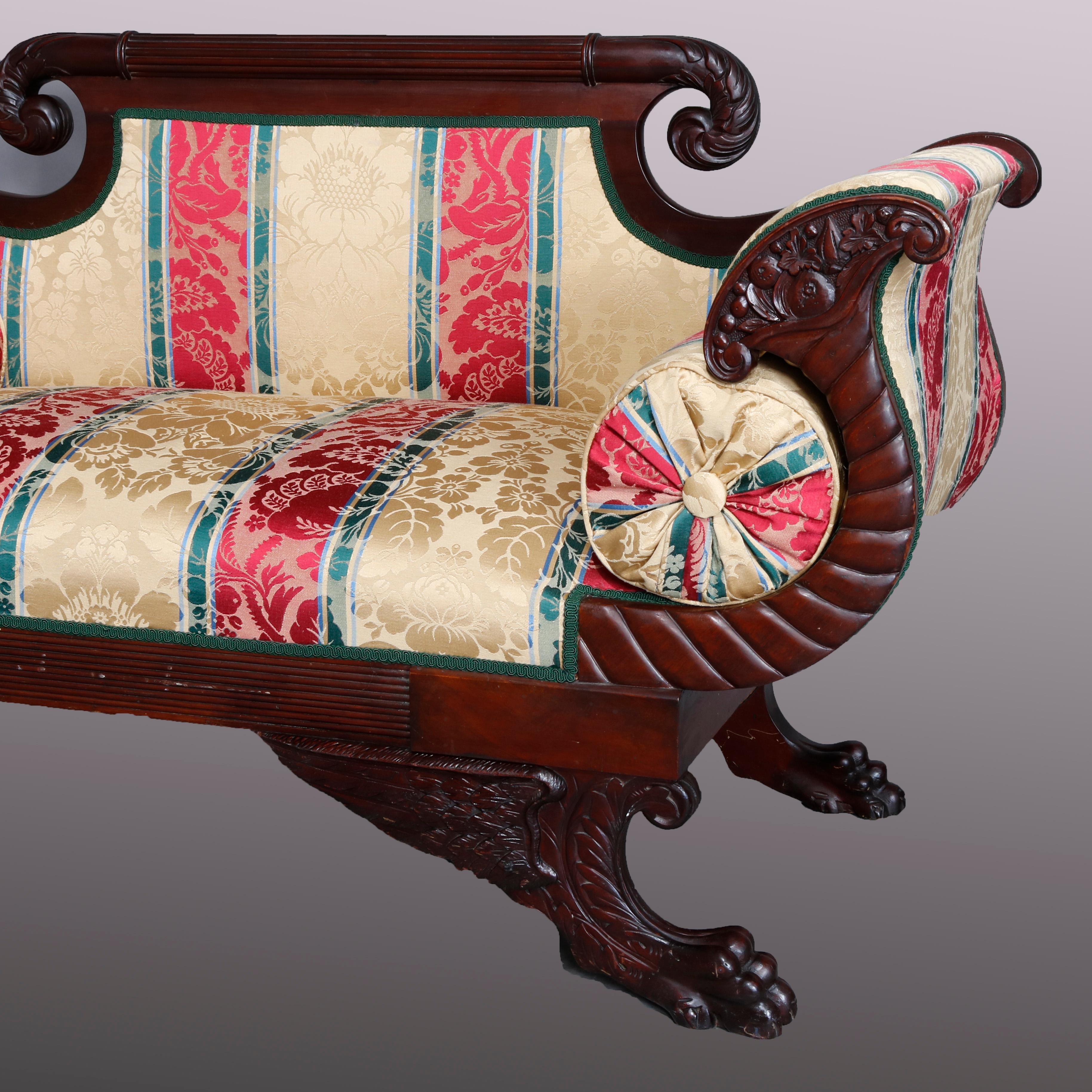 An antique American Empire settee offers flame mahogany construction in Classical form with scroll form crest surmounting upholstered back and seat, flanked by cornucopia form arms and raised on carved winged paw feet, circa 1830.

***DELIVERY