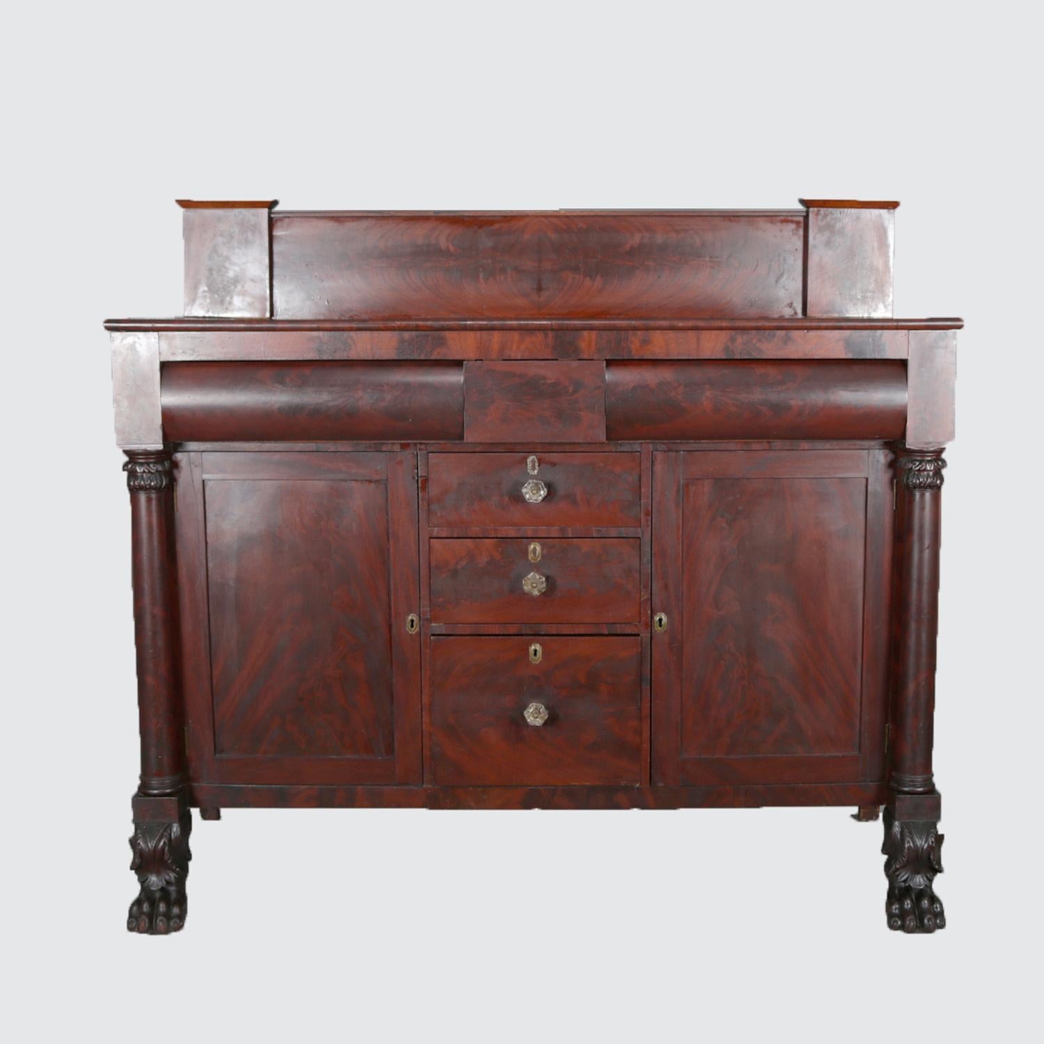 An antique Classical American Empire flame mahogany sideboard features serving platform with backsplash surmounting case with two upper convex drawers over three stacked central drawers flanked by side cabinets and full Corinthian column-form