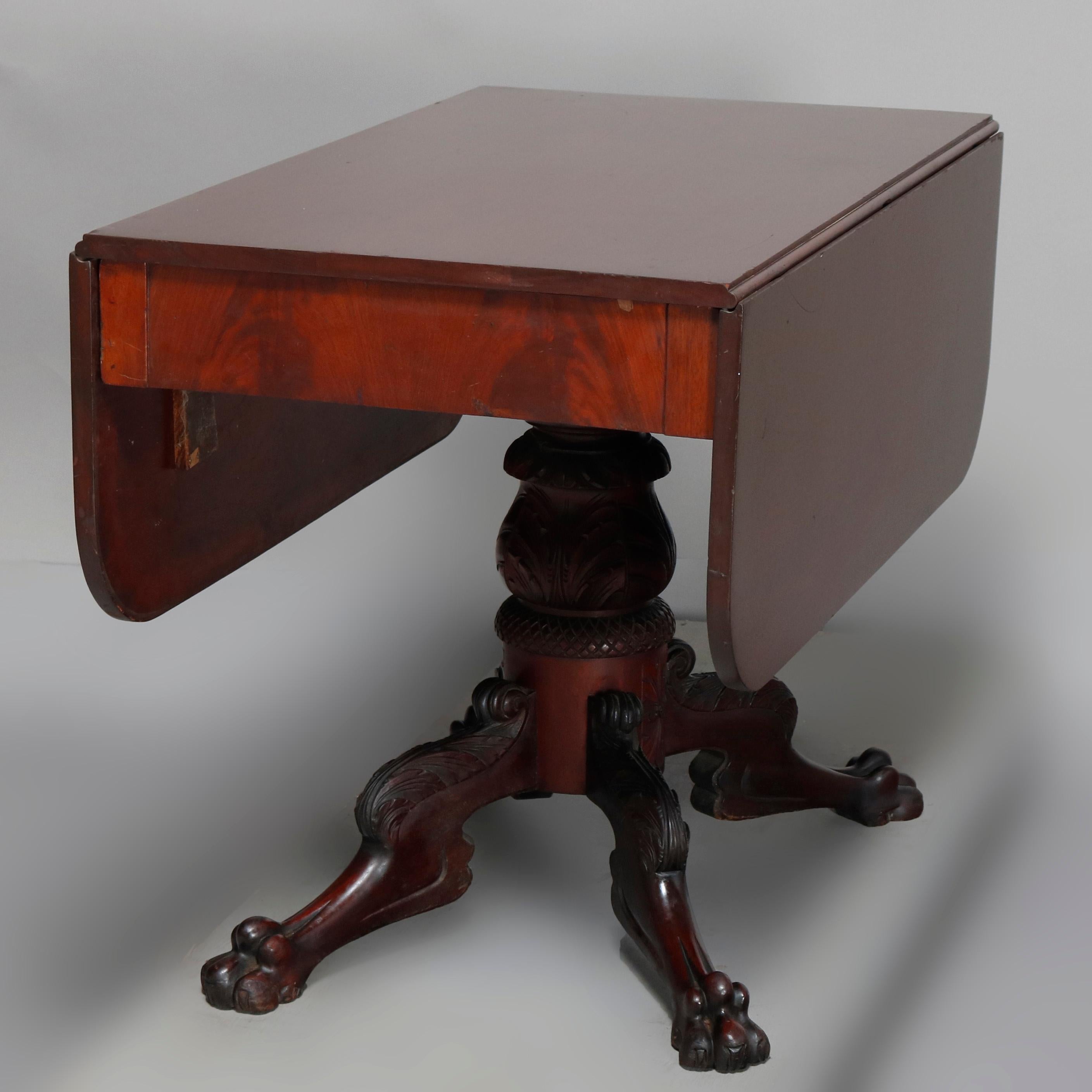 An antique classical American Empire drop-leaf table offers mahogany construction raised on acanthus carved pedestal having carved paw feet, circa 1850

Measures: 28.75