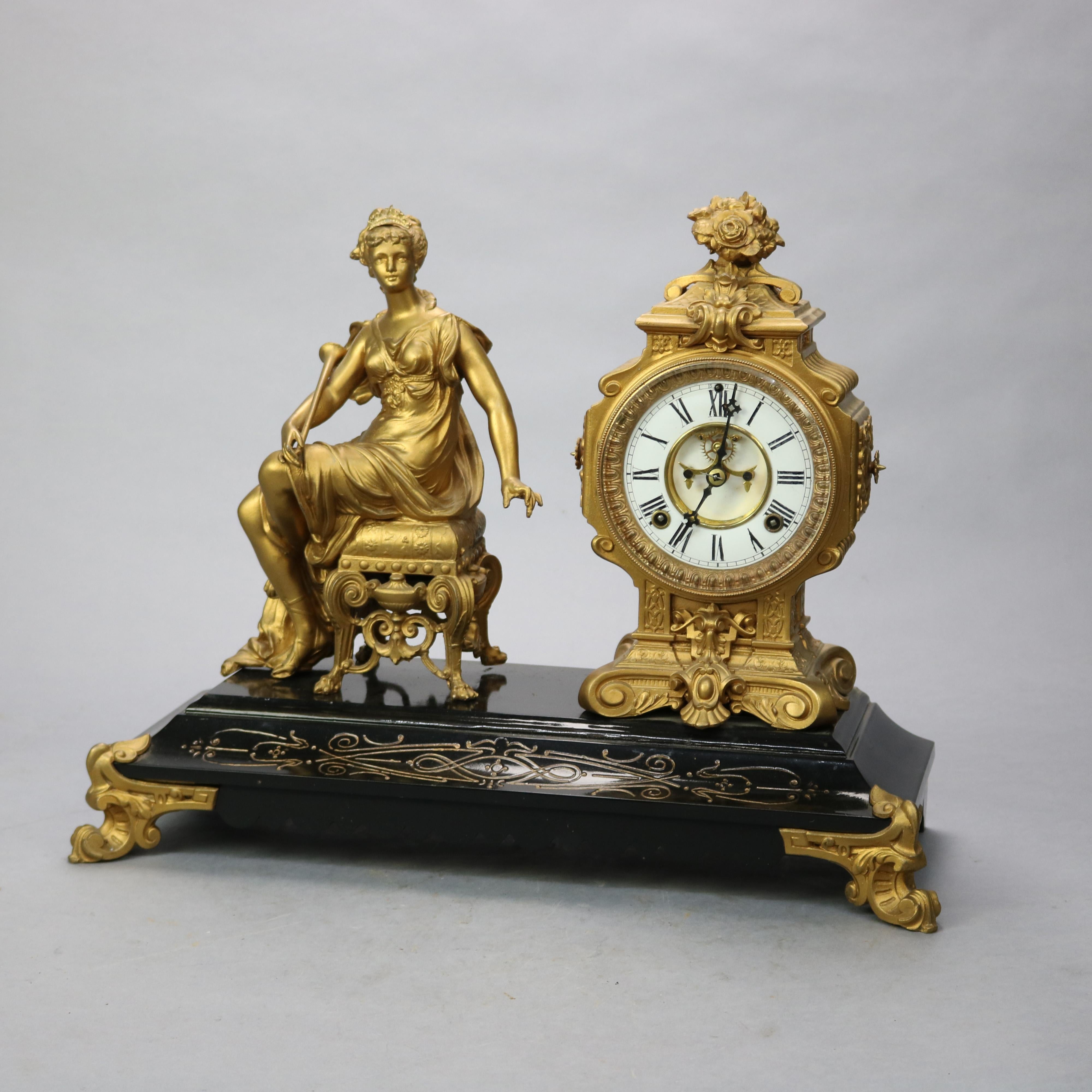 An antique figural mantel clock by Ansonia offers bronzed Classical Woman seated on an ornate stool and holding a horn beside a clock having a panier de fleur finial and raised on scroll feet, all seated on a slate base with incised and gilt scroll