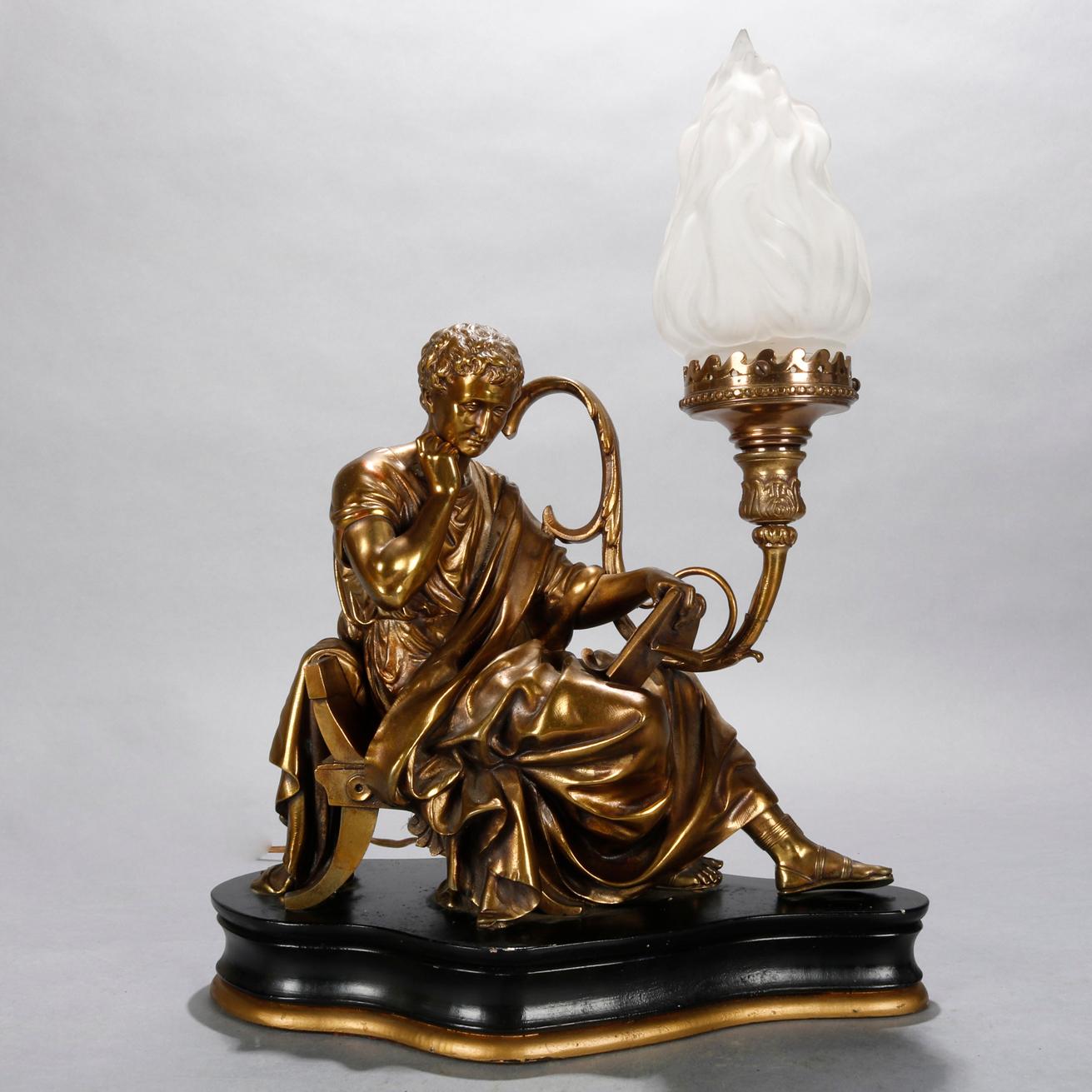 An antique Classical table lamp offers bronzed sculpture of recumbent robed man (scholar) with scrolled foliate form lamp terminating in light with flame form glass shade and seated on shaped ebonized wood base having gilt banding, working and wired