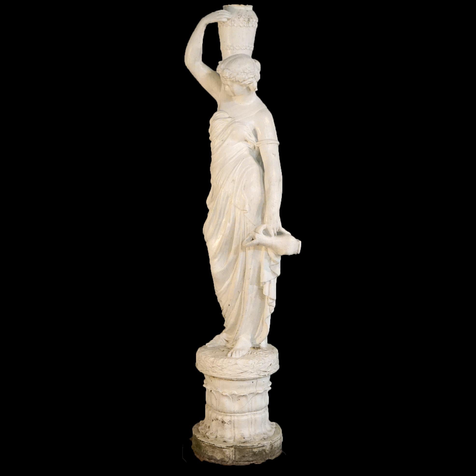 An antique Classical garden fountain offers cast hard stone construction with portrait of a standing woman with her water gathering vessels, raised on circular base, 20th century

Measures- 65''H x 16''W x 12.25''D.