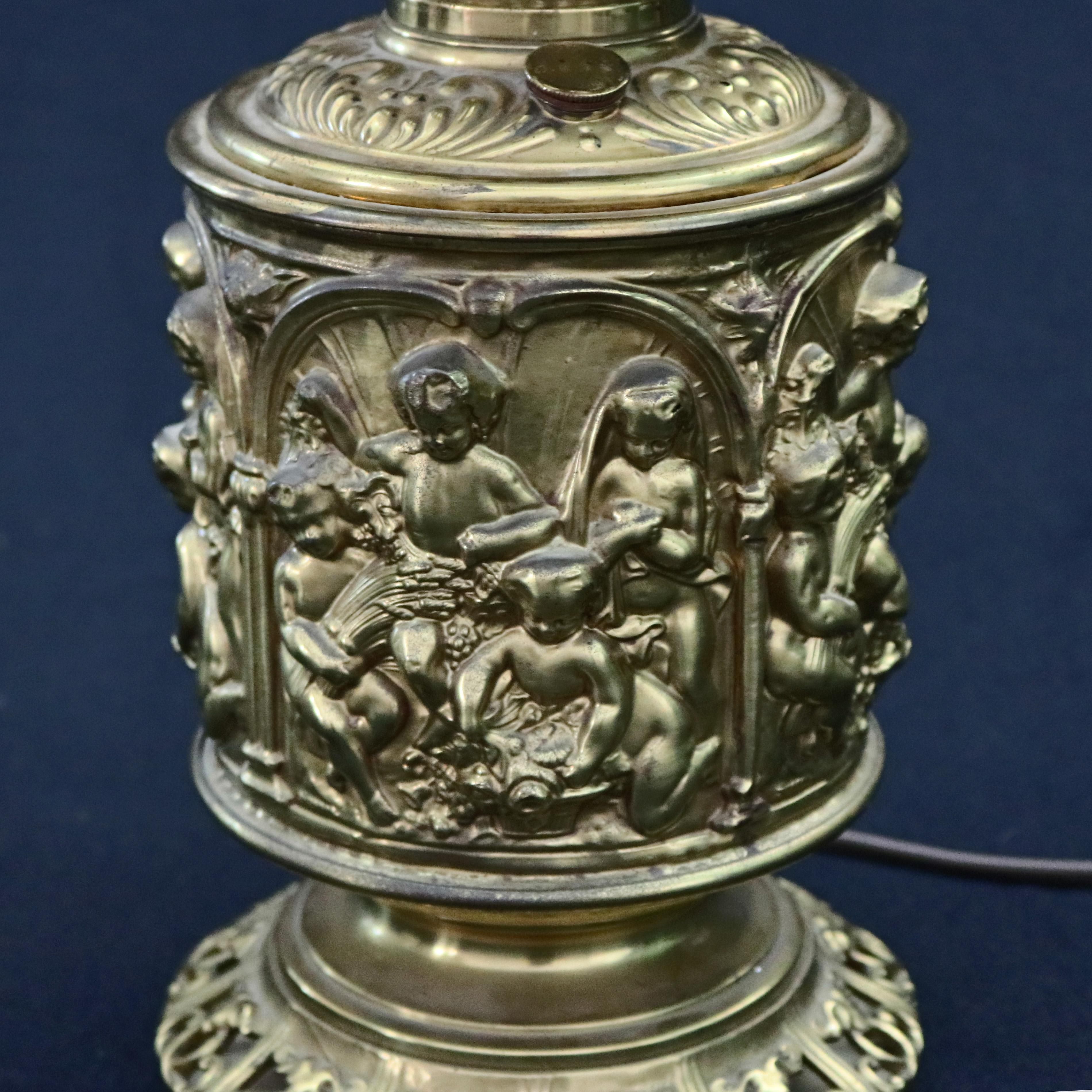 An antique gone with the wind parlor table lamp offers high relief embossed brass classical cherub scenes raised on pierced foot and surmounted by hand painted floral globe, electrified, 19th century

***DELIVERY NOTICE – Due to COVID-19 we are
