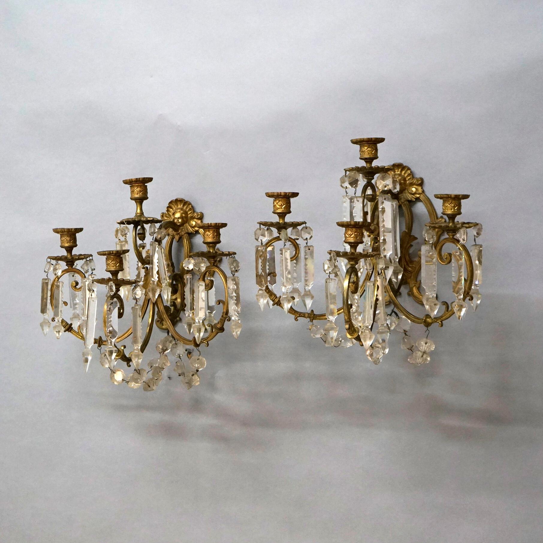 An antique pair of French wall sconces offer cast and gilt bronze construction with central cherub masks, three scroll form arms terminating in candle sockets, and cut crystal highlights throughout, 19th century

Measures- 13.5''H x 14''W x 12.75''D