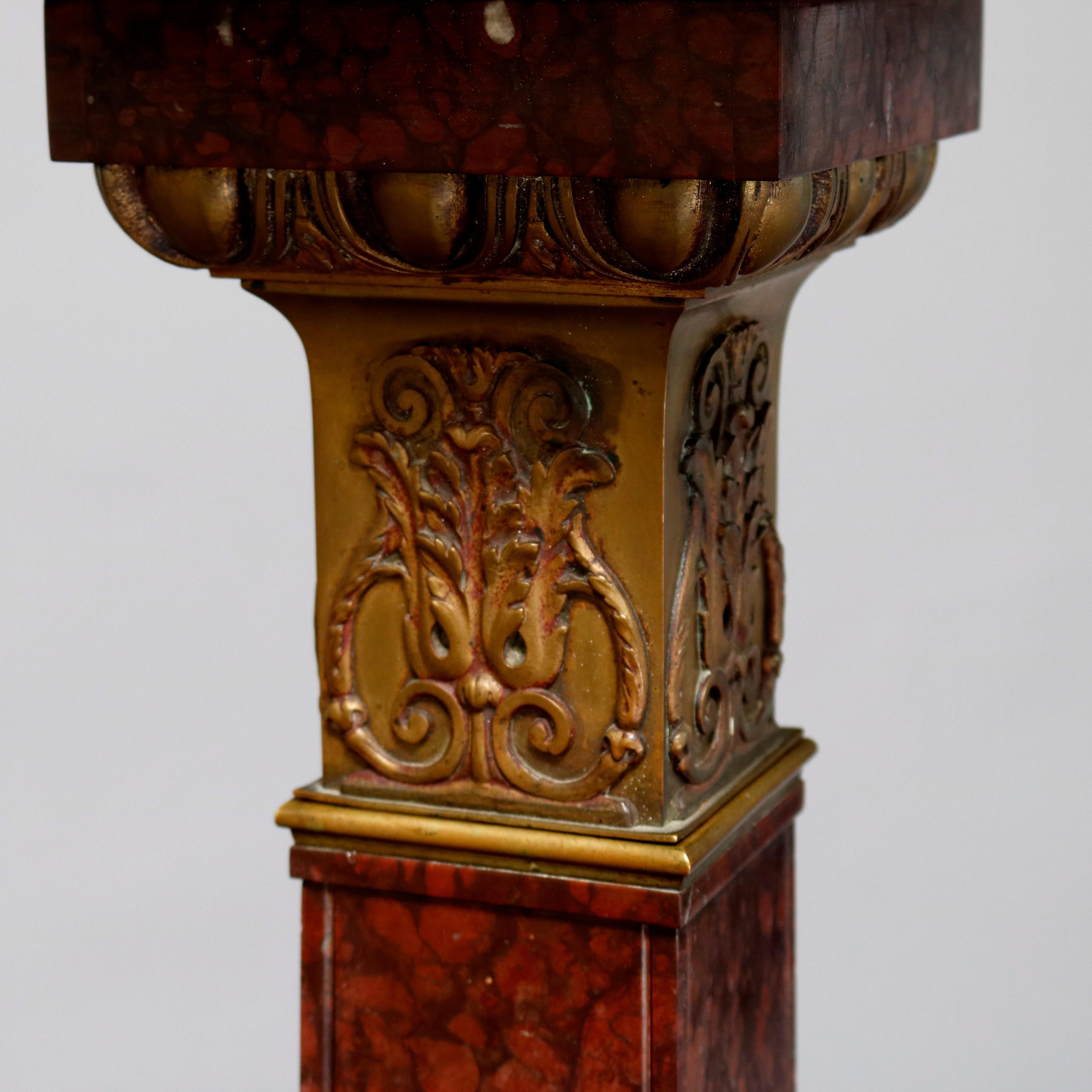 An antique classical Italian rouge marble sculpture display pedestal offers stylized Corinthian column form with cast scroll and foliate bronze capital and stepped base having cast bronze rosettes, foliate banding and having and feet, circa