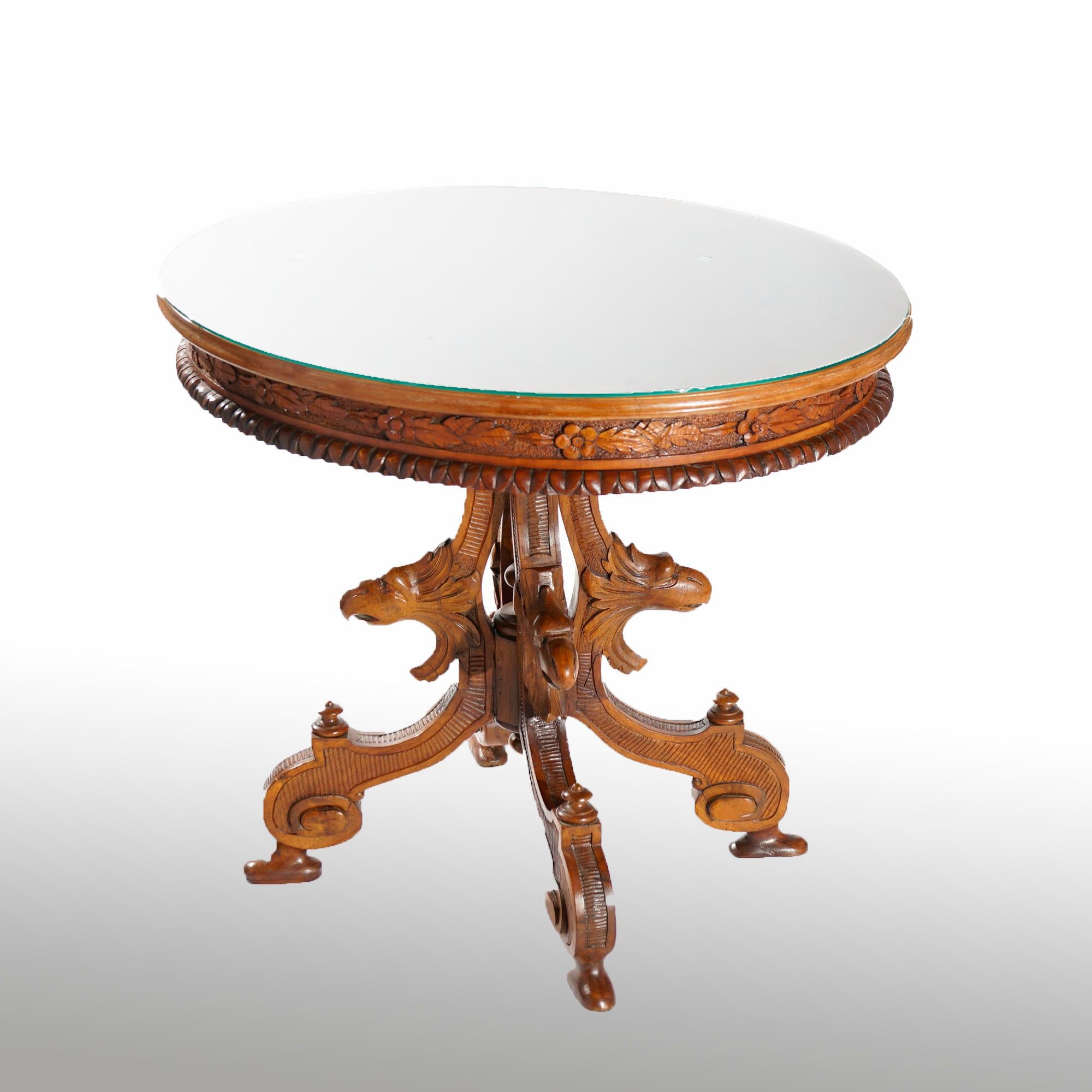 An antique Classical center table offers marquetry inlaid top having central cherub playing a flute in countryside setting with floral and foliate surround over carved skirt, raised on cabriole legs with figural carved eagle or phoenix heads