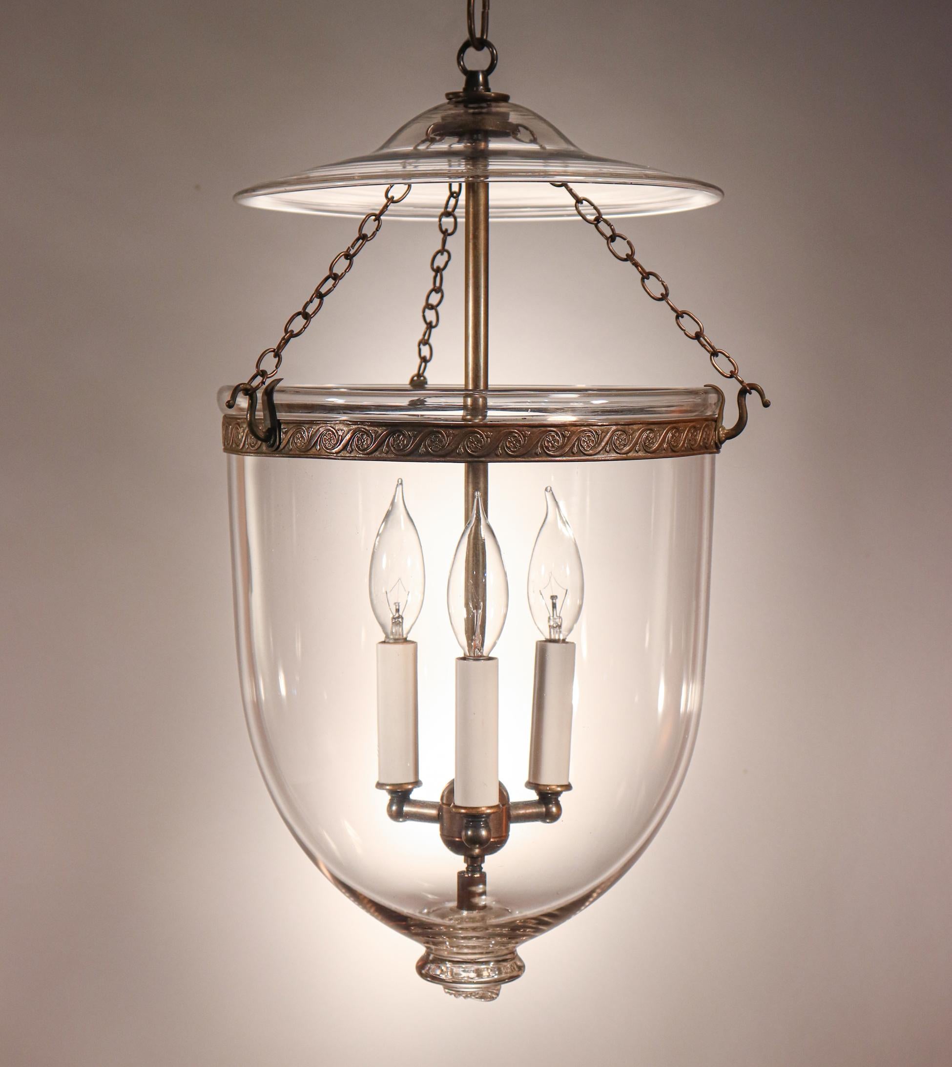 An antique bell jar lantern from England with excellent quality hand blown glass and attractive form. This circa 1870 lantern also has its original brass band with an embossed floral motif. It has been newly electrified with a three-bulb candelabra