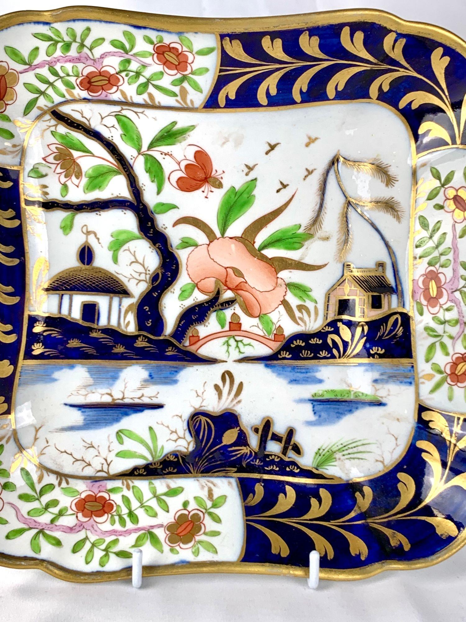 Diese antike Porzellanschale aus Coalport, die um 1820 in England hergestellt wurde, hat eine quadratische Form mit sanft gekerbten Ecken und einem schön ausgewogenen handgemalten Imari-Dekor.
Die zentrale Szene zeigt stilisierte Pavillons in einer