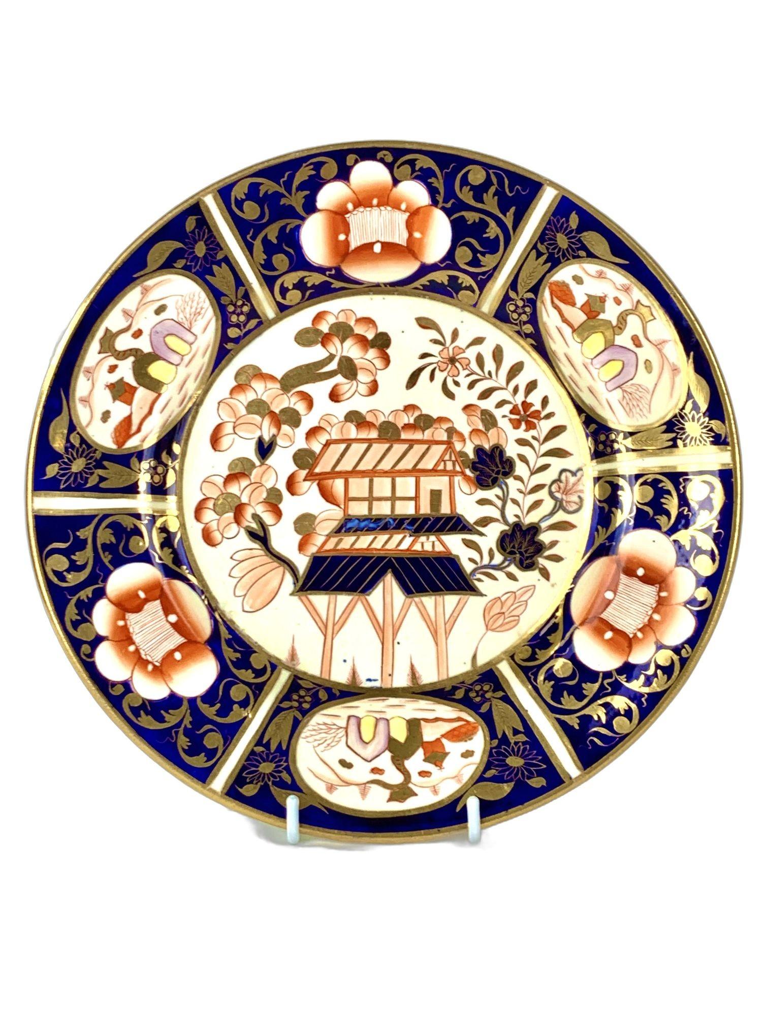 This antique porcelain plate was hand-painted by Coalport in England around 1820.
It features a lovely central scene of a two-tiered pagoda set within a garden, surrounded by flowering branches.
The decoration is rendered in a vibrant English Imari