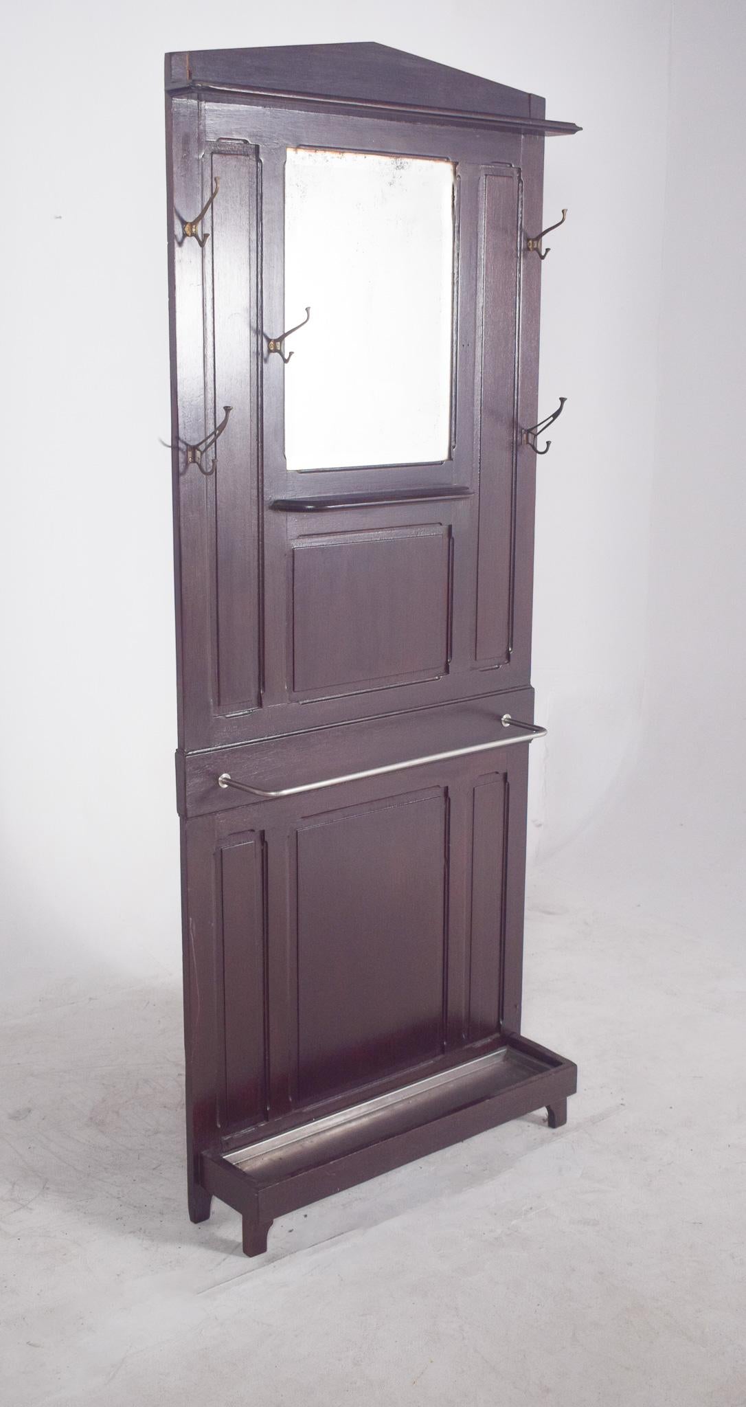 Perchero con espejo. Una pieza funcional y robusta, ideal para entradas o pasillos. De madera oscura, su diseño es sobrio y utilitario, con líneas rectas y paneles moldeados que le dan cierta estructura decorativa, aunque discreta.
En el centro hay