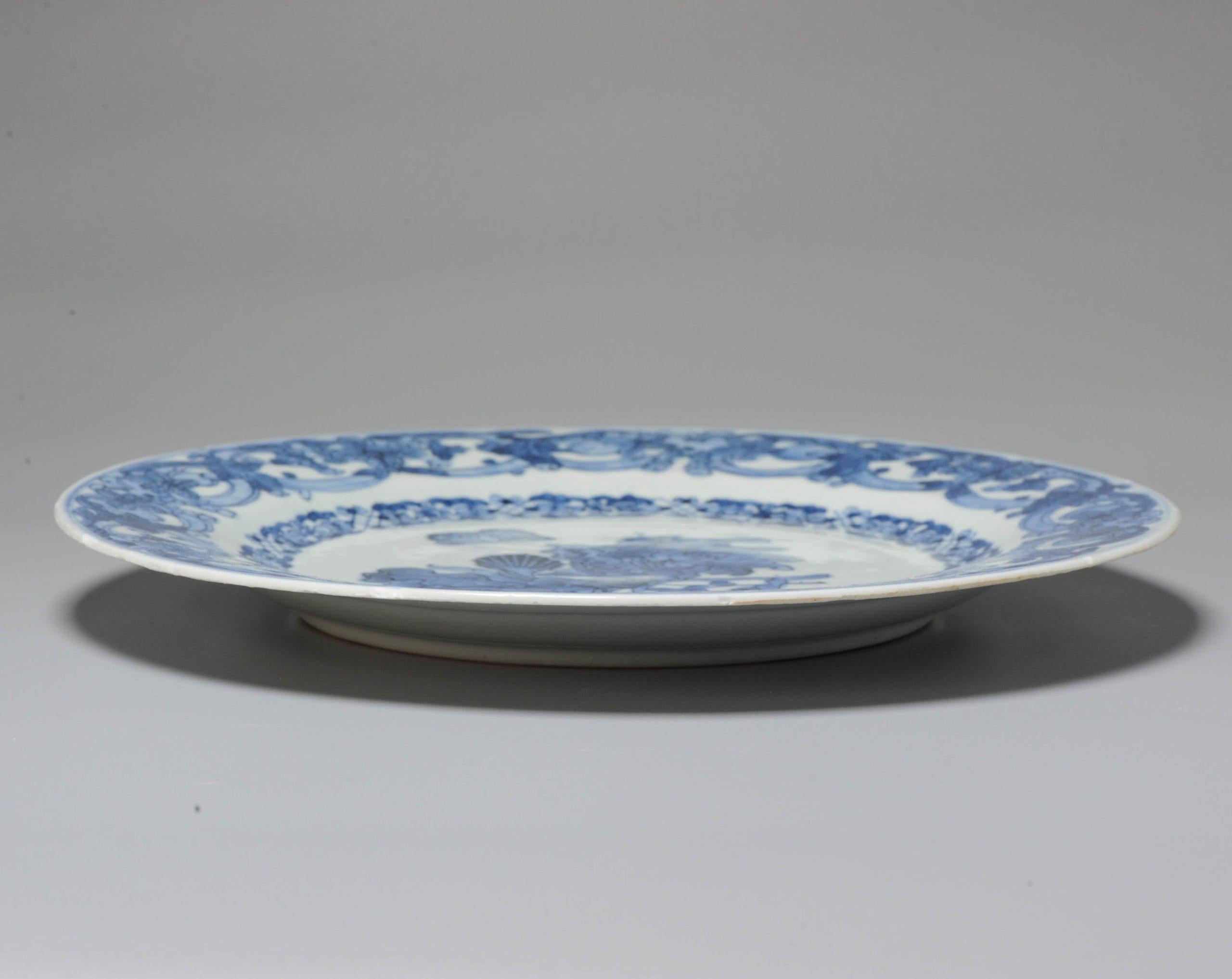 Larger dish on footring, flat rim. Decorated in underglaze blue with a butterfly and two flowers (iris and anemone). On the anemone, a large caterpillar. A second caterpillar is found on a lower leaf. The cavetto is encircled by a decorative border