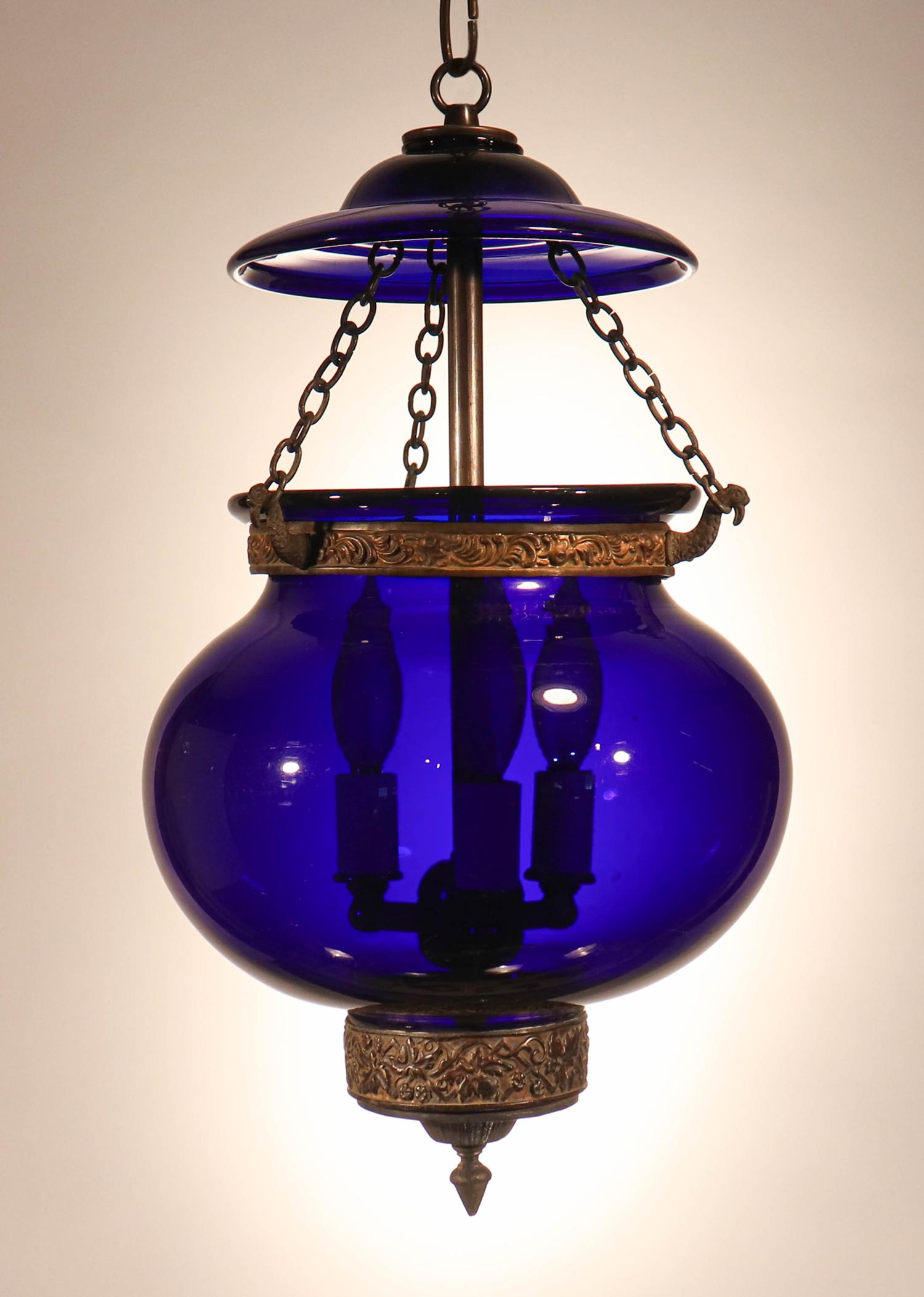 A deep, cobalt blue hand blown glass globe bell jar lantern from England, circa 1860. This authentic antique pendant features its original brass band, chains and finial/candleholder base. Please note that the very bottom of the bottom portion of the