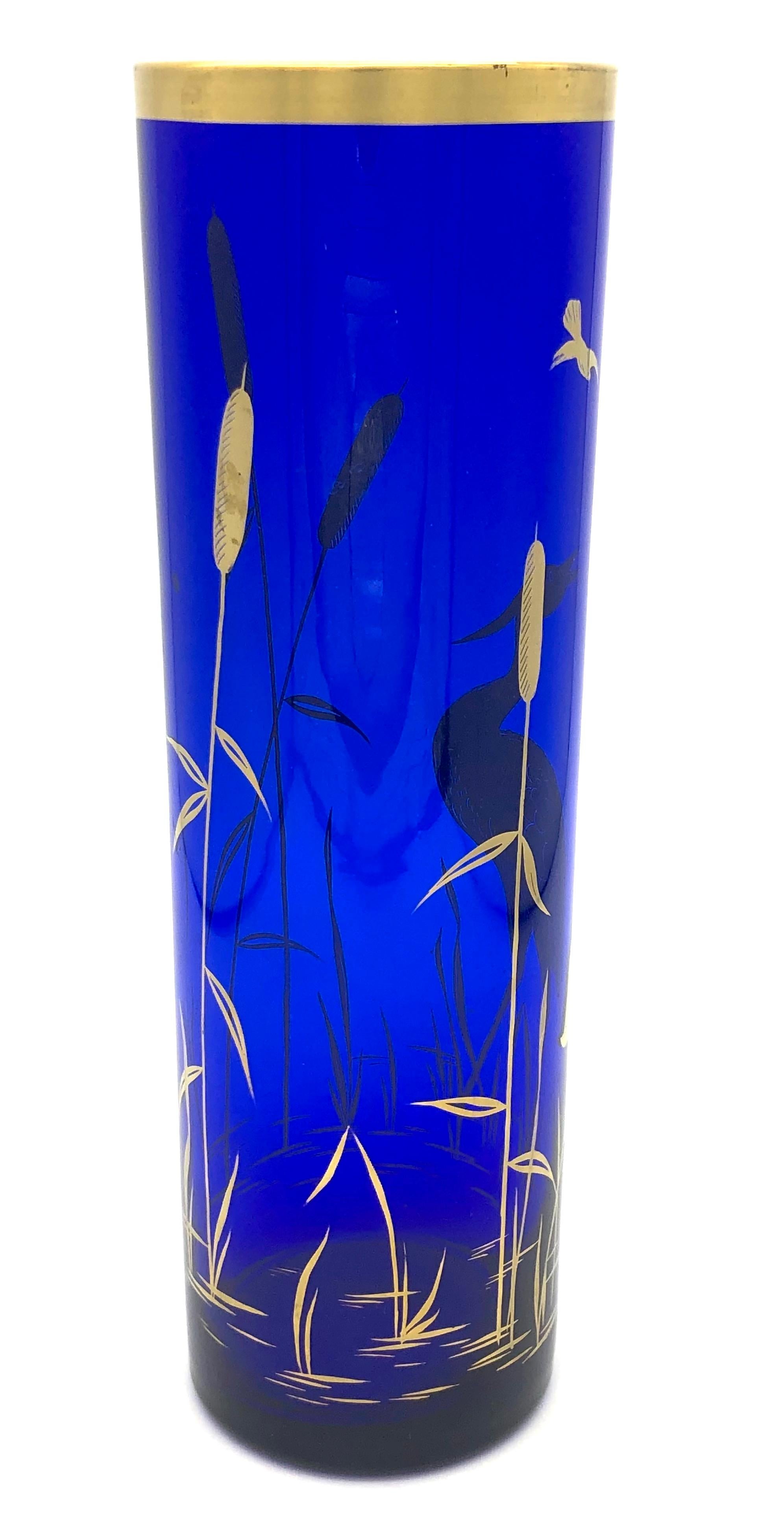Cet élégant vase en verre bleu cobalt de forme cylindrique est peint à la main avec de l'émail doré, représentant une scène avec une grue dans une rive de roseaux. Dans les arts et l'artisanat asiatiques, la grue est un symbole de longévité et de