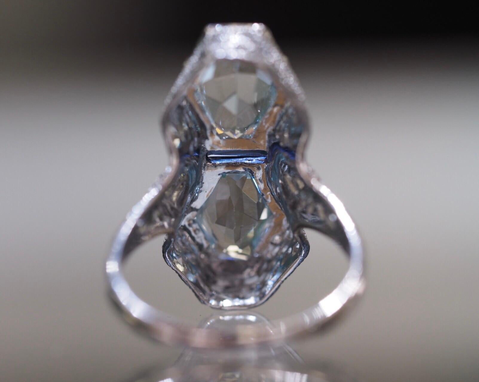 This antique aquamarine ring is hand crafted to perfection. It has two hexagonal natural aquamarines with a lab grown rectangular sapphire bezel set right in the center. The entire mounting is lavishly adorned with fine open filigree scroll-work and