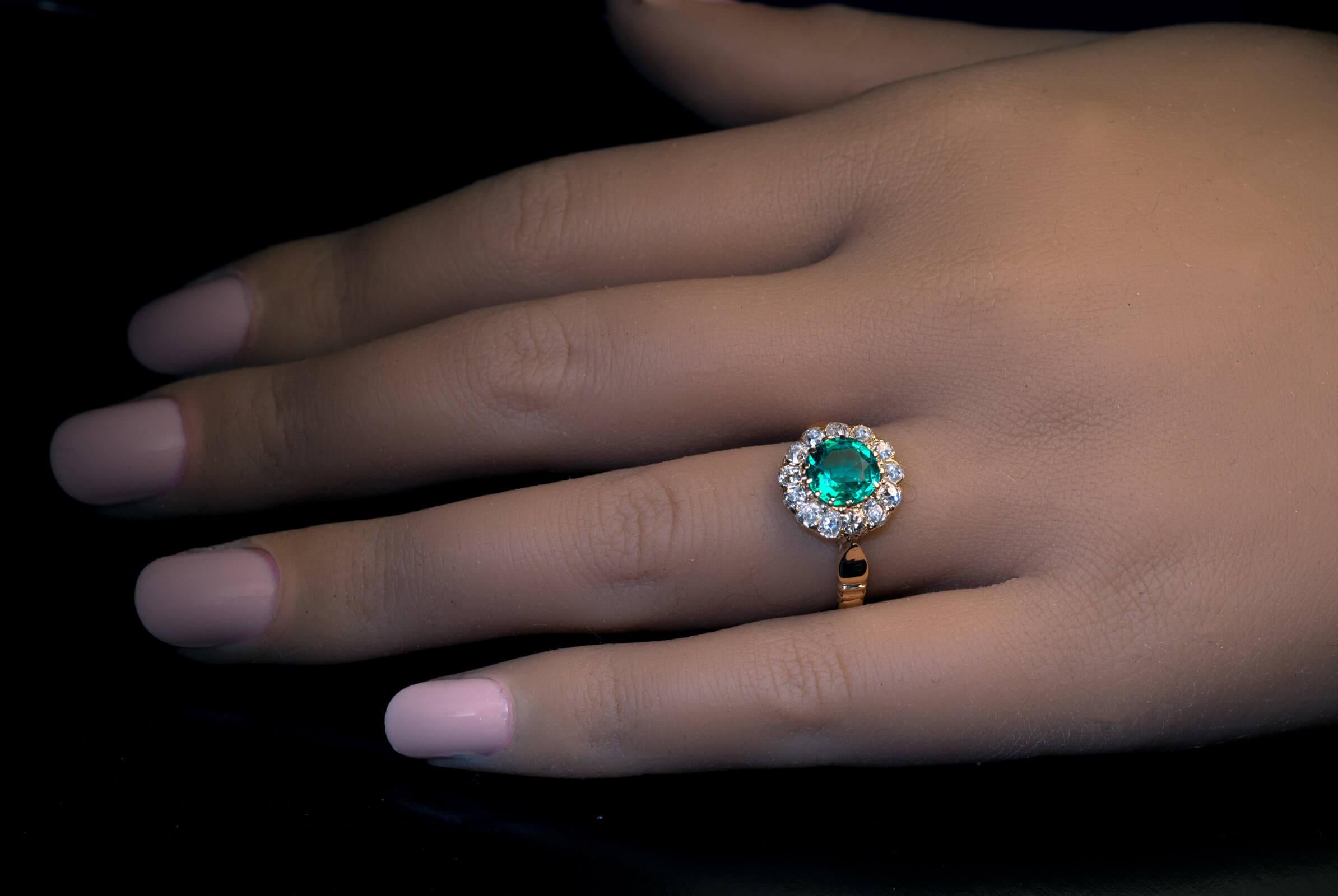 Circa 1900  This classic antique 18K gold cluster ring is centered with an excellent bluish green 1.09 ct Colombian emerald surrounded by bright white old mine cut diamonds (G-H color, SI clarity). The round cut emerald is eye clean (very rare for