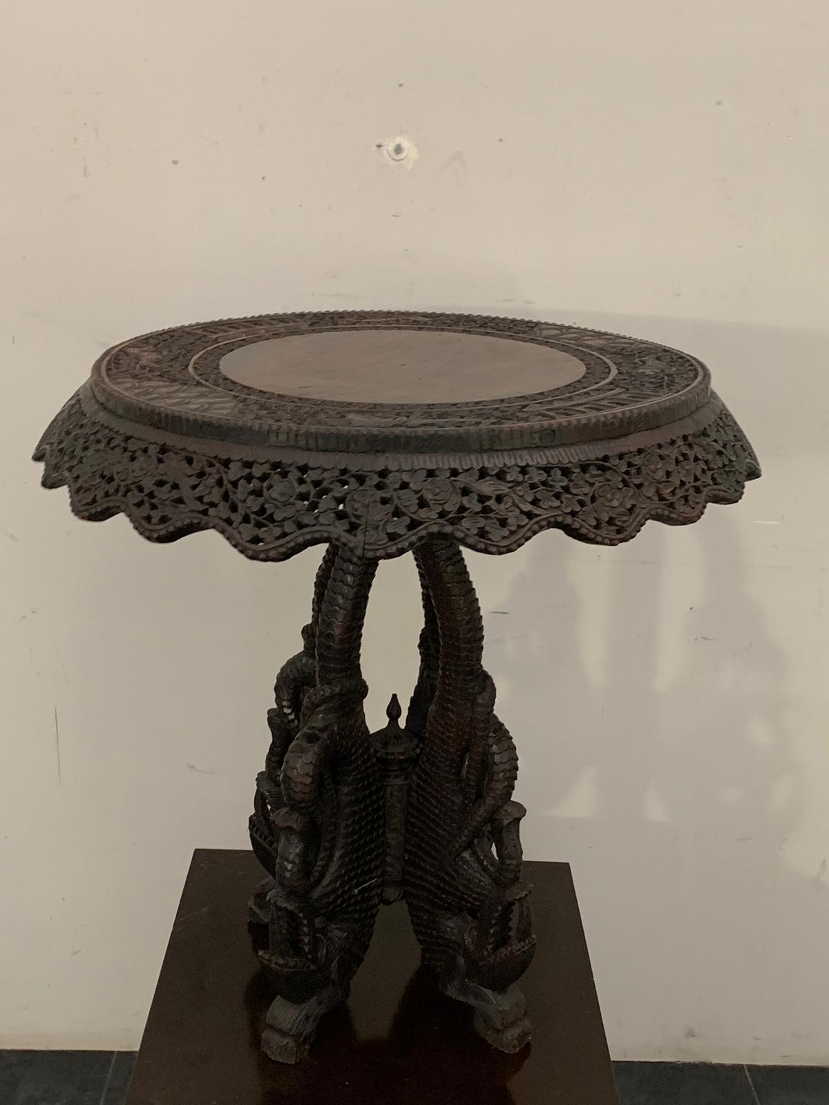 Tea table, Anglo Indian colonial, the base is carved with grotesque marine, the top edged with skirt is carved with flowers and foliage, the top is rotatable and it is deduced that it was prepared for a tet a tet, small parts and hand forged