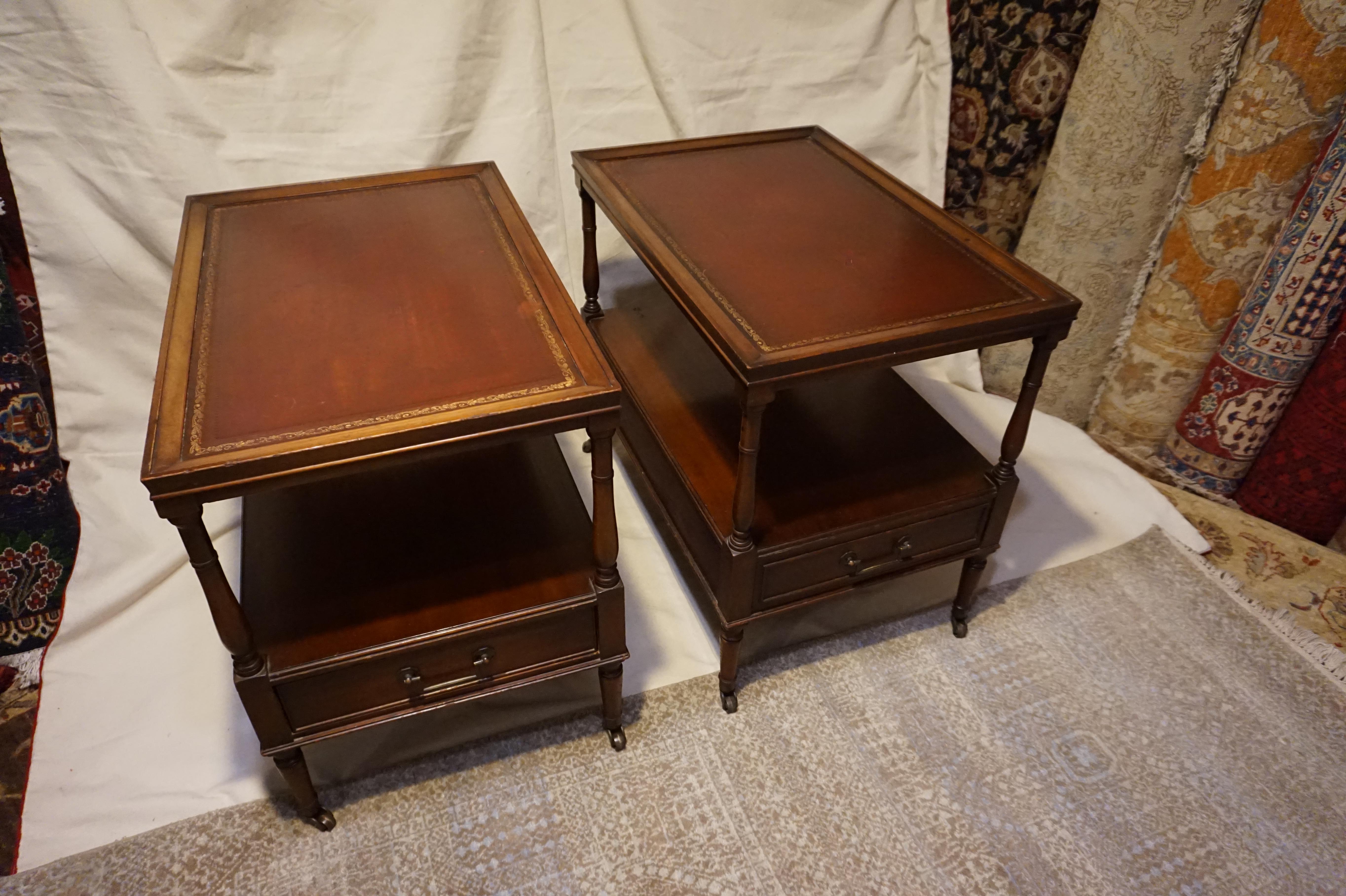 Solid mahogany handcrafted American Colonial Style side tables with gilt leather tops and single drawers and shelves. Original brass hardware including brass casters. Good sturdy condition with the character of age. Some wear visible consistent with