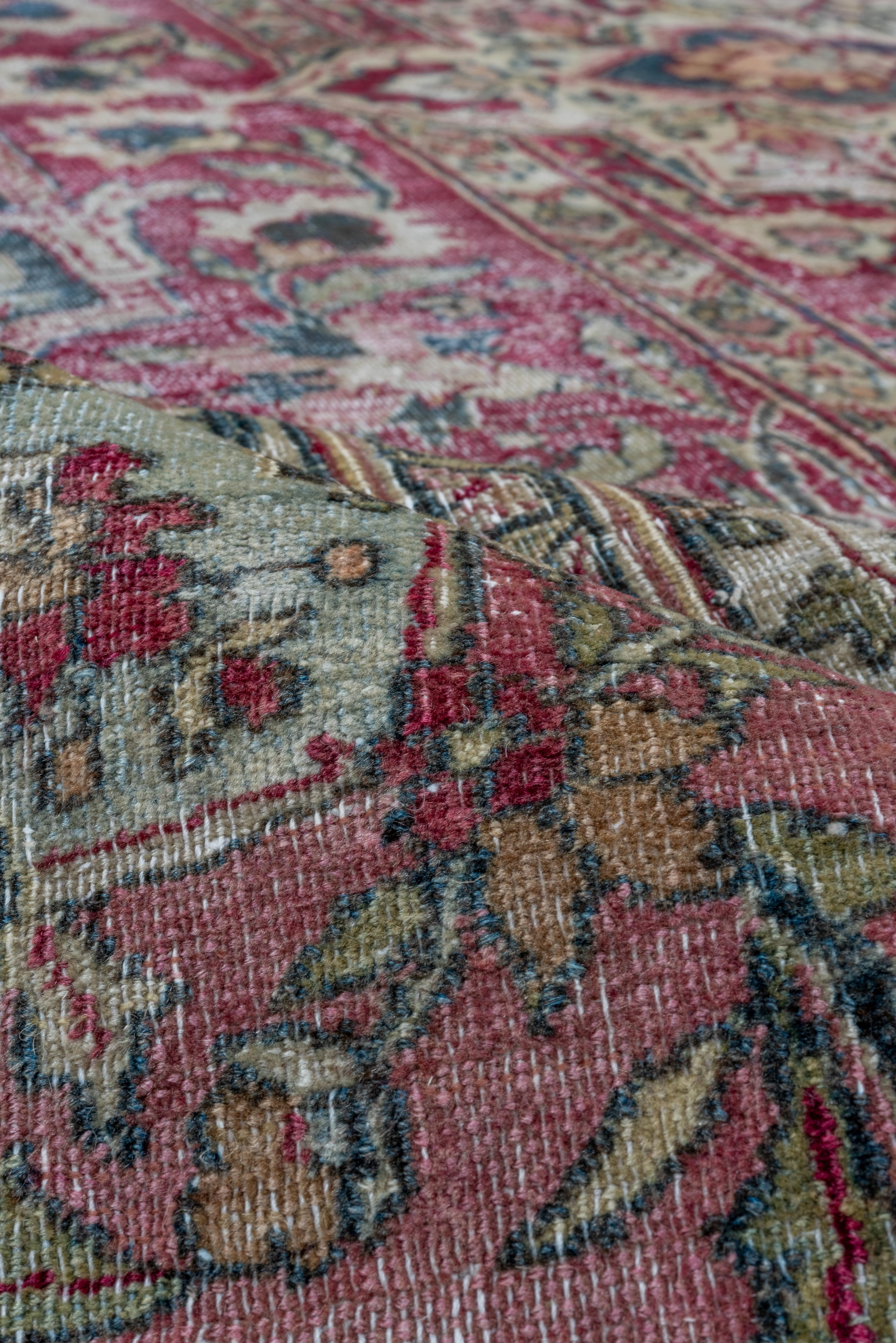 This somewhat distressed northeast Persian carpet shows a wine red cartouche enclosing an ivory reversed acanthus edged ivory eight radiating palmette medallion steadied by partial poles at each side. Dark green surrounding field. Ivory medallion
