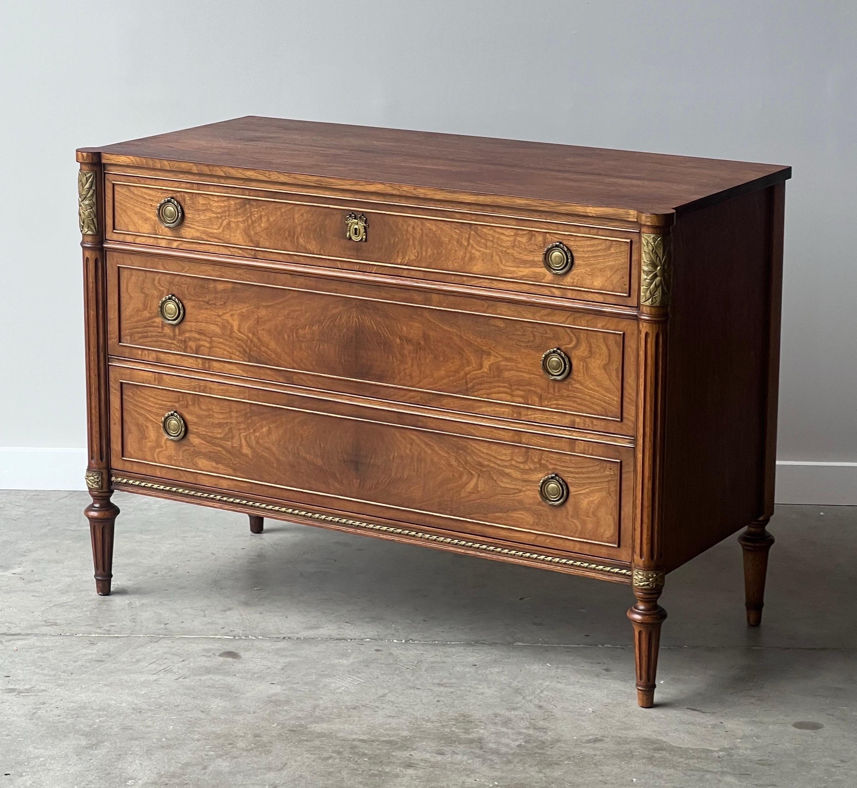 Antique French style three drawer chest / entry commode made by Robert Irwin of Irwin Furniture. Extremely ornate with turned wooden legs, carved flowers, decorative brass handles, and a spiral inlay. Each drawer varies in size and is beautifully