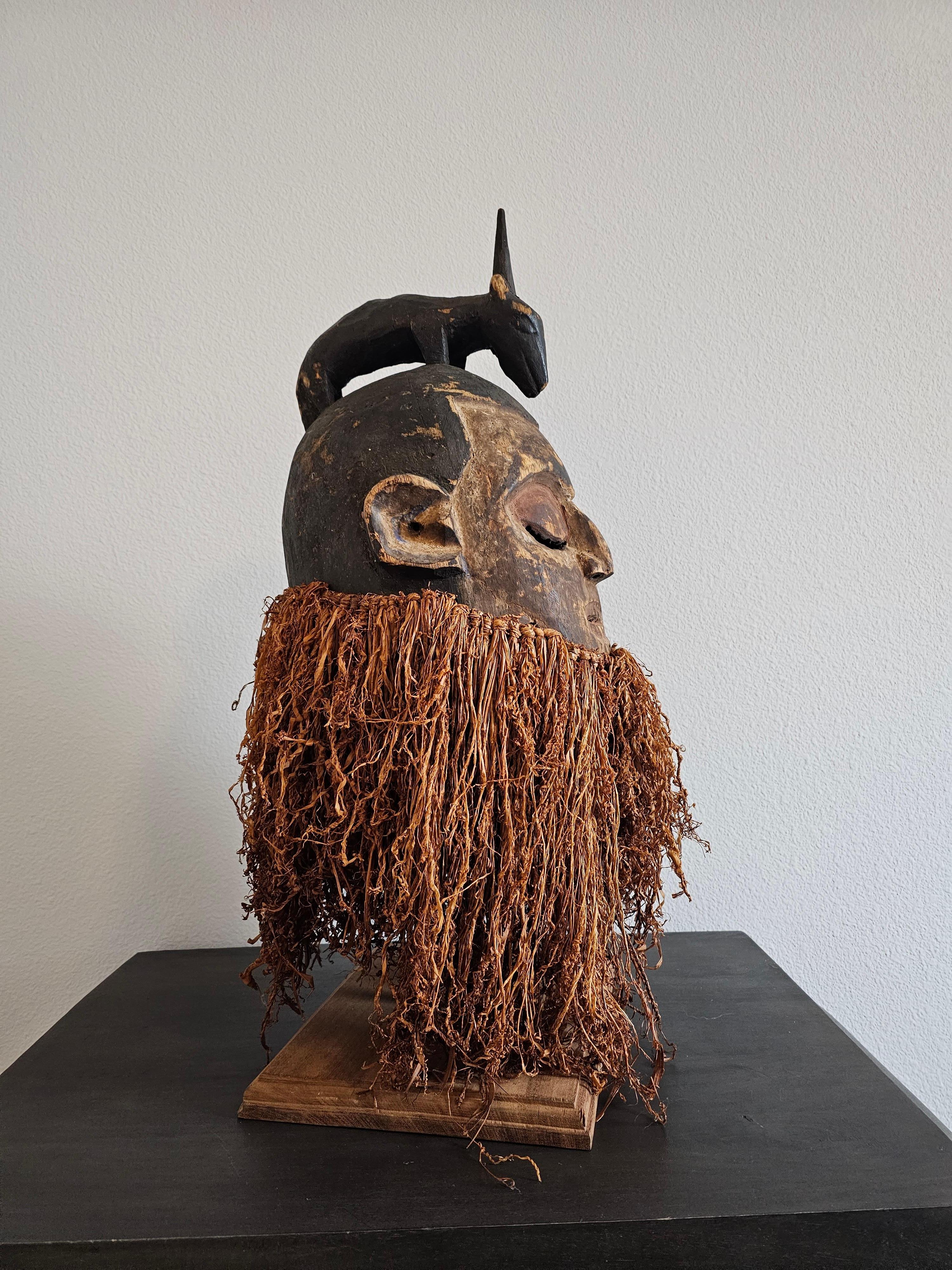 A scarce antique African tribal carved Hemba helmet mask, the Suku peoples, possibly Kwese culture, Democratic Republic of the Congo, Central Africa, early 20th century, surmounted by four-legged animal, over round face, with mouth ajar and incised