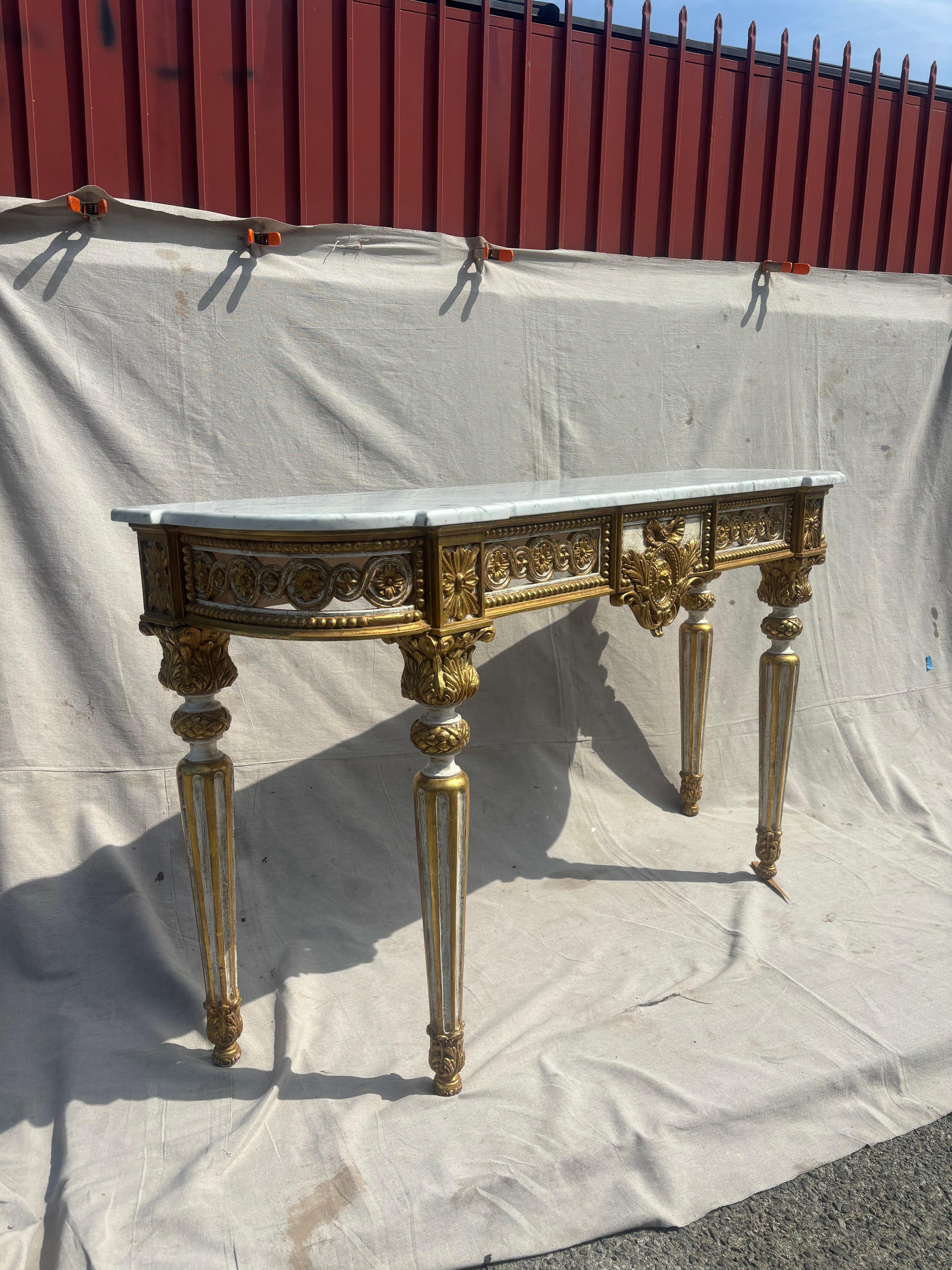 Fabriquée avec une attention méticuleuse aux détails, la console présente un cadre en bois finement sculpté, orné de motifs classiques qui reflètent l'influence néoclassique de l'époque. Le cadre est recouvert d'une délicate patine vieillie, ce qui