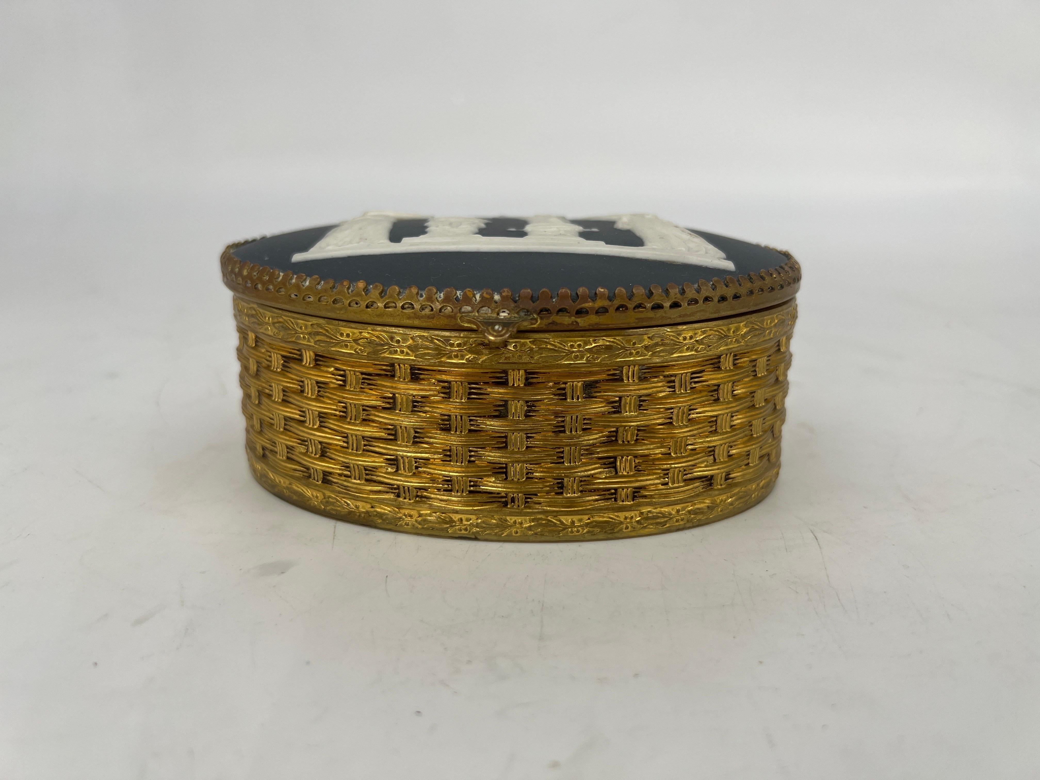 Continental, early 20th century.

A antique oval box made of brass and other metals. The box has a basketweave pattern to the exterior and an affixed basalt plaque to the top. The plaque has not been taken off the box to examine the maker. Otherwise