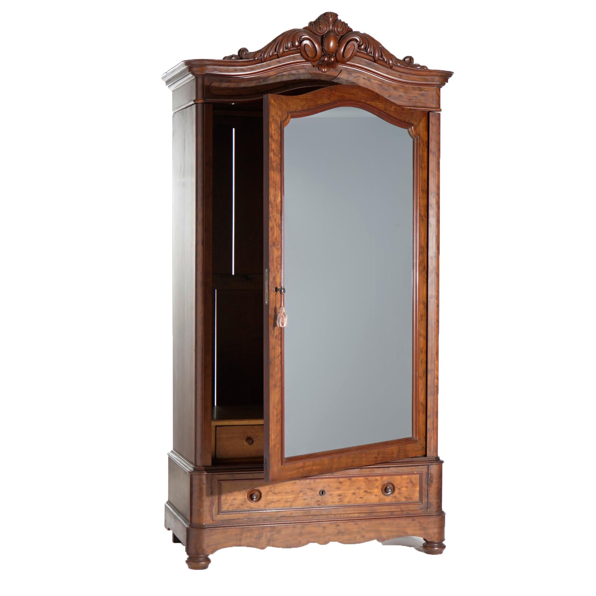 An antique Continental armoire offers flame mahogany construction with arched top having carved foliate and shield crest over case having single mirrored door and lower long drawer, raised on bun feet, c1880

Measures- 92''H x 46.25''W x