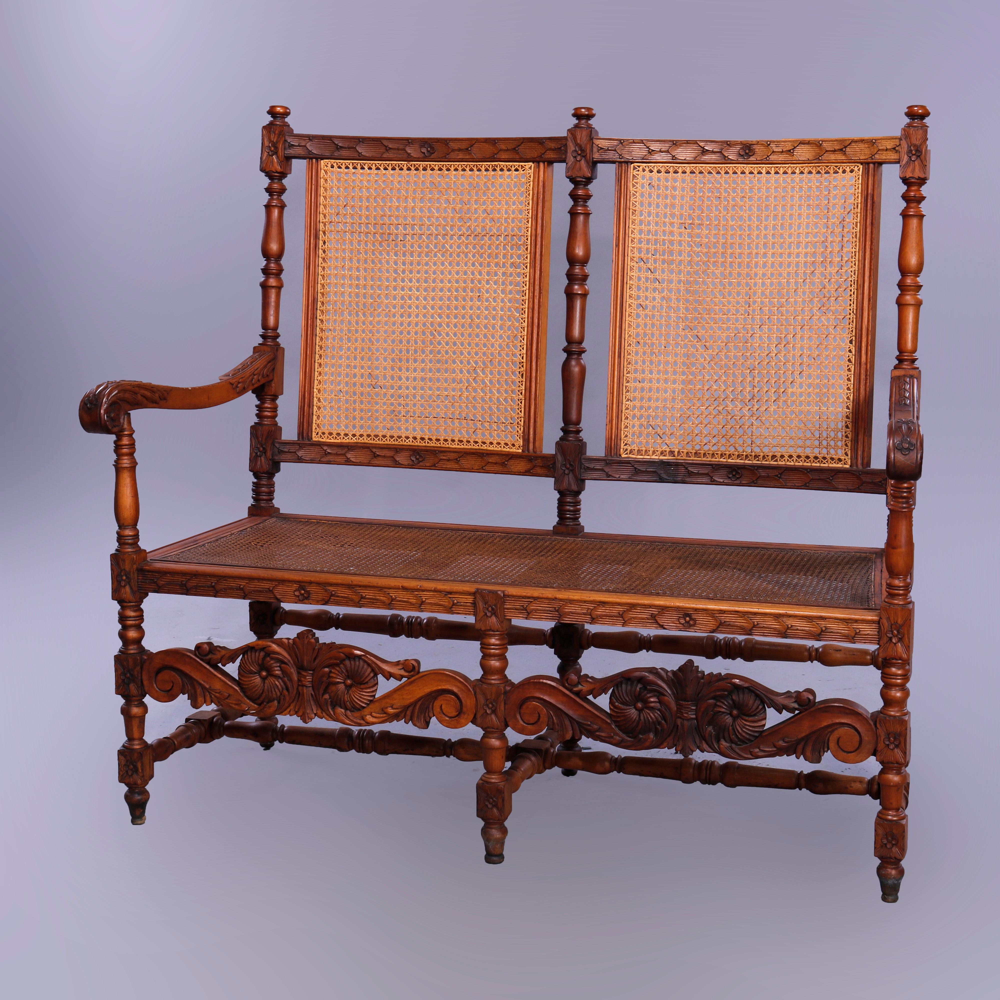 An antique Continental Edwardian settee bench offers walnut frame with carved foliate elements, cane back and seat, carved acanthus scroll form arms, raised on turned legs having rosettes and caved floral stretcher, c1900

Measures - 46.5''W x