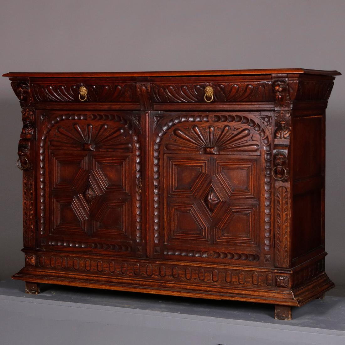 An antique Continental figural hunt sideboard offers paneled oak construction with carved gadrooned drawers with cast lion pulls surmounting lower double door cabinet having deeply carved stylized sunburst over central rosette medallion having