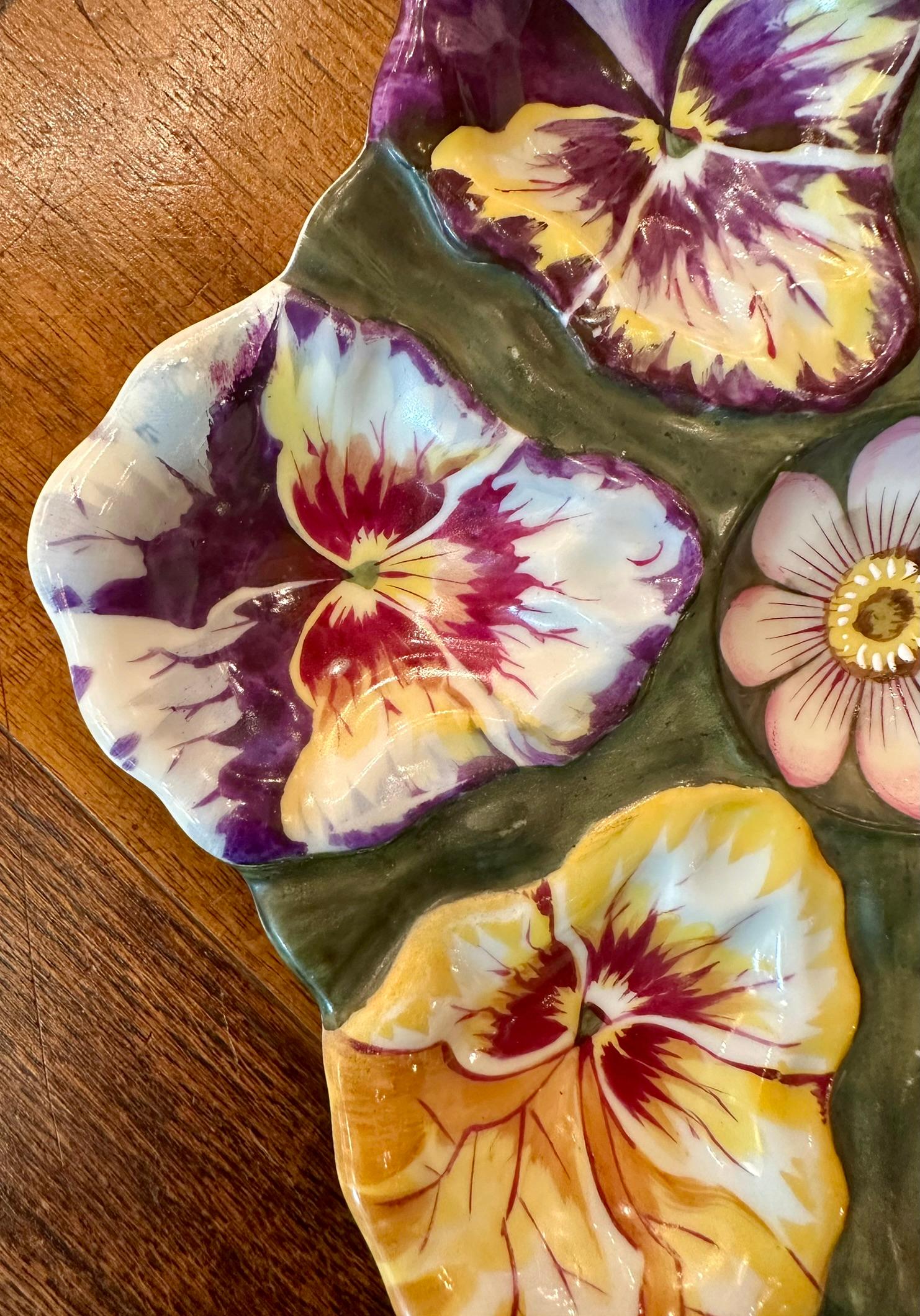 Raro piatto da ostriche antico in porcellana continentale dipinto a mano con il disegno di una viola del pensiero, circa 1900-1910.
Dipinto con bellissimi colori audaci di viola, fucsia, giallo, rosso e verde bosco.