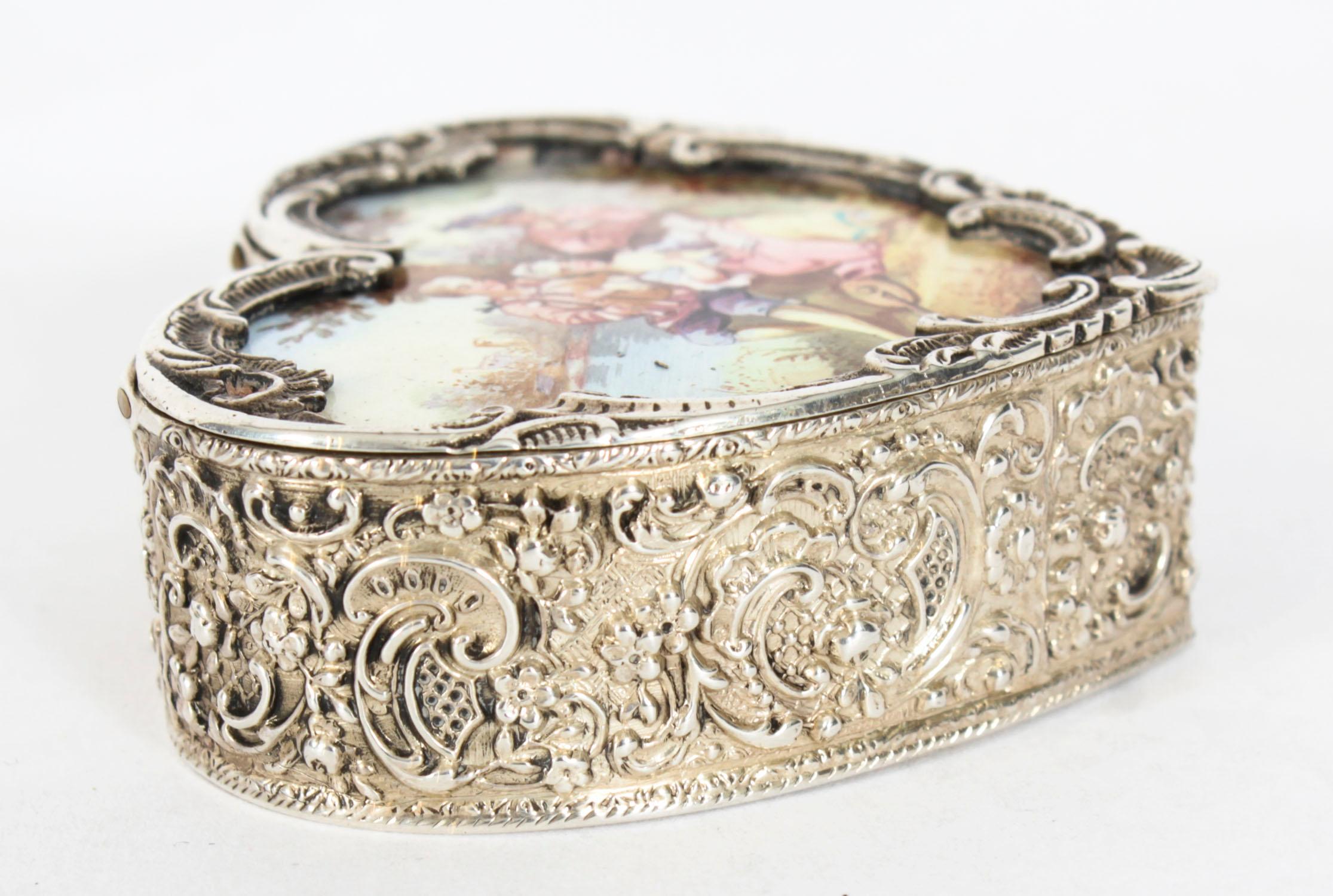 This is an exquisite antique continental silver and enamelled heart shaped pill box marked .900 silver, circa 1920 in date.

The pill box is of heart shaped form with embossed foral decoration, it features a hand painted enamelled top of a musician