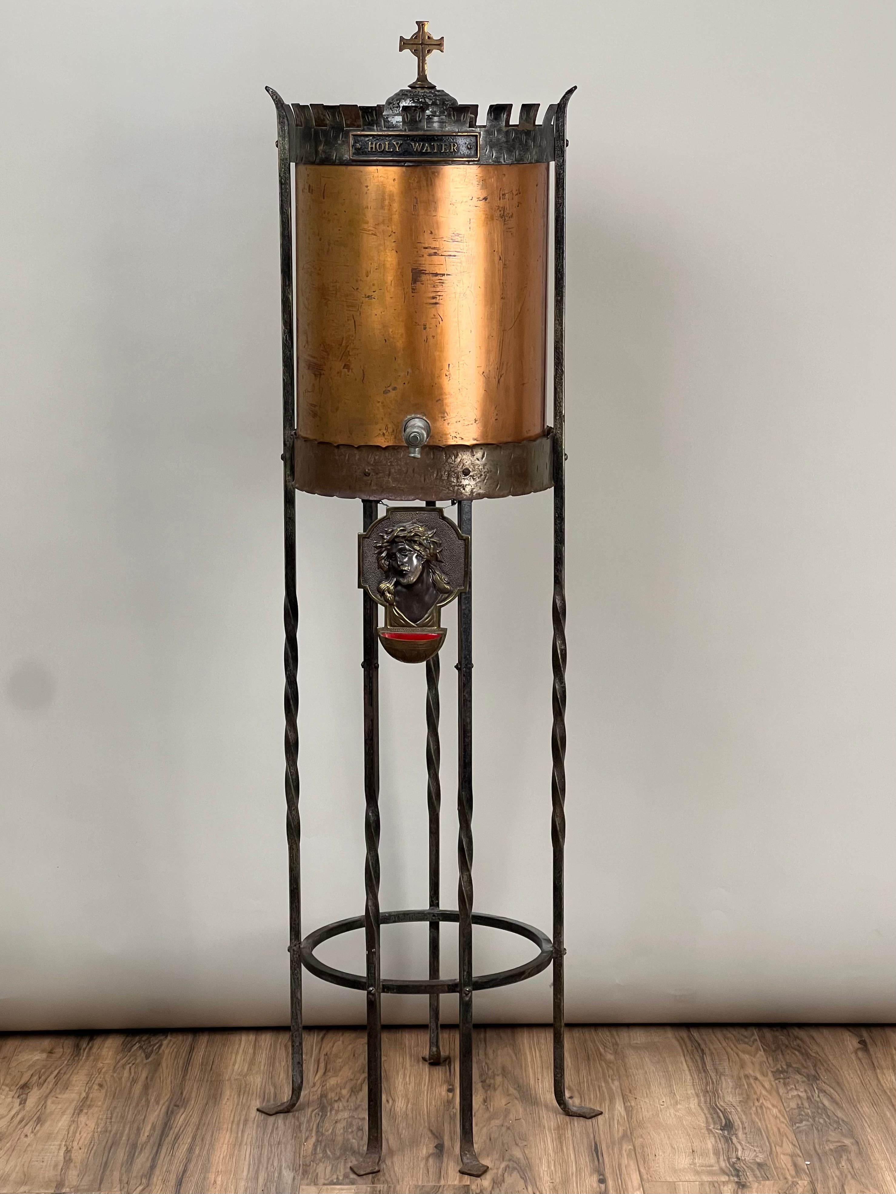 Questo antico dispensatore di acqua santa in rame e ferro battuto, risalente al 1900 circa, è un pezzo sorprendente che unisce il design funzionale al simbolismo religioso. Realizzato in rame massiccio, il dispenser ha sviluppato nel tempo una