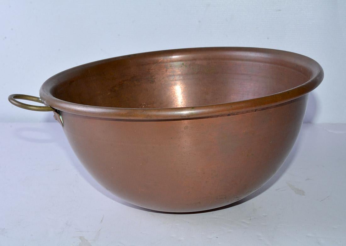 The antique copper bowl has a curled rim, a deep cavity and a ring for hanging. Decorative and for centerpieces.