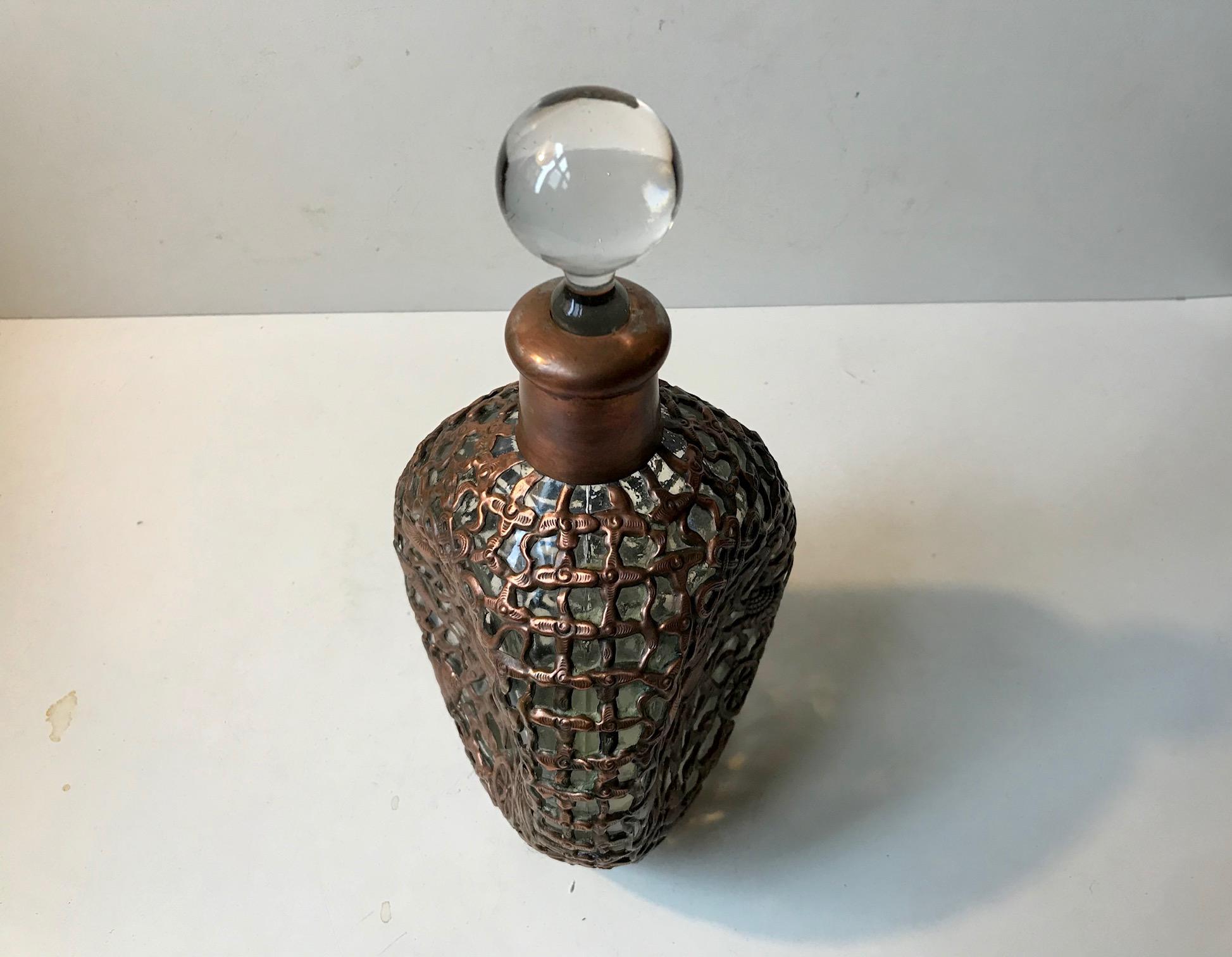 Unusual glass decanter. It has collapsed sides and is caged in copper. Motifs of celtic symbolism transends all sides. It was probably made in the UK somewhere between 1850-1900. Although antique it has an almost modern brutalist appearance.
It has