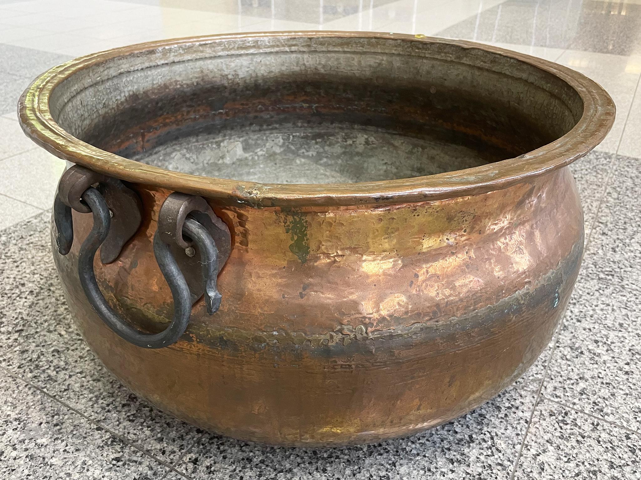 This large, antique cauldron is made from hammered copper with wrought iron handles. It stands out for its luster, beautifully tactile surface, and the variety of color in the metal's patina.

Dimensions:
24.5 in. diameter
14.5 in.