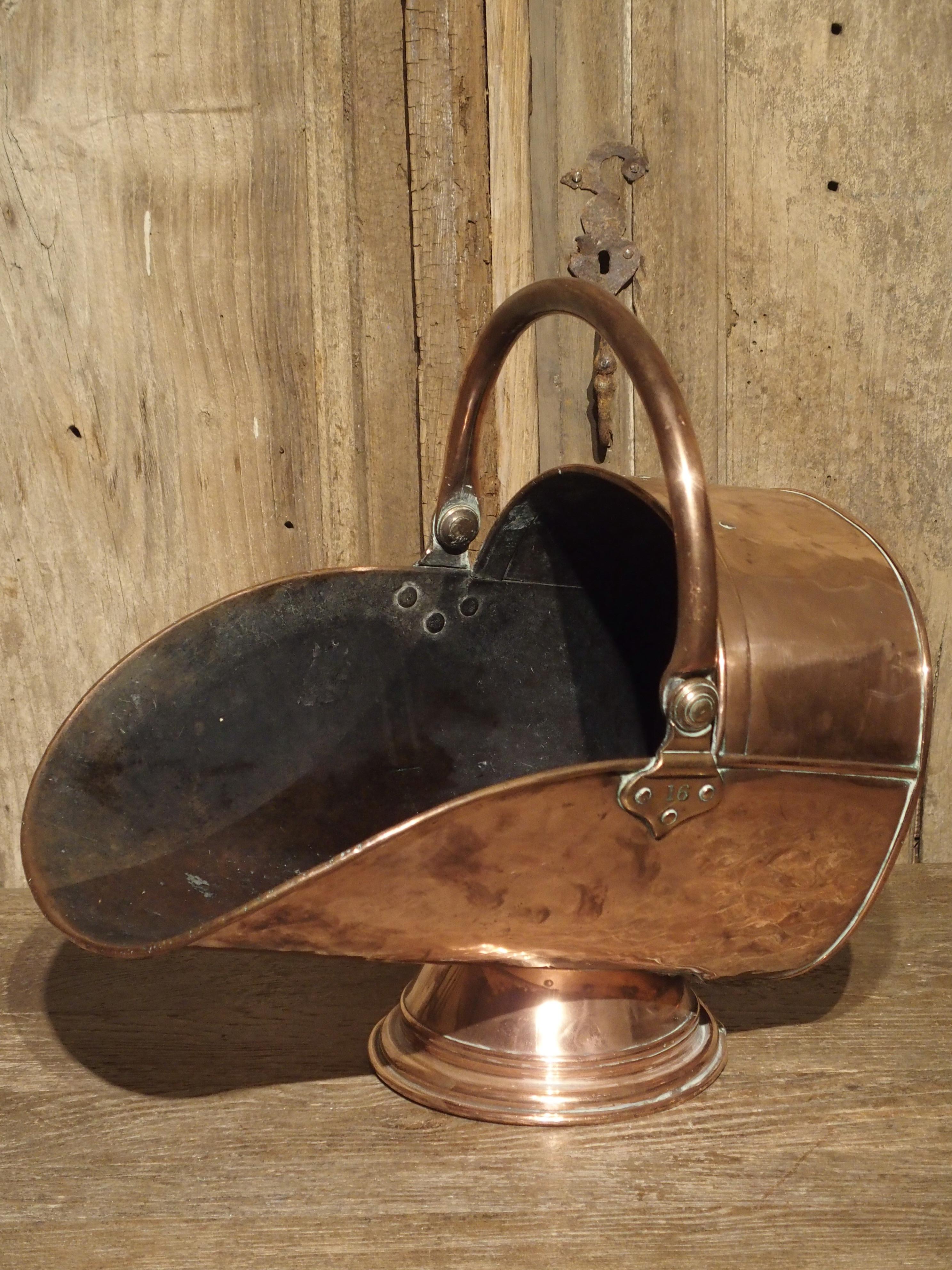 This beautiful antique copper coal scuttle from England was made in the 19th century yet still retains a vibrant color and is in good condition. It has a large copper handle and the scoop portion measures over 18 inches. The number 16 is on the side