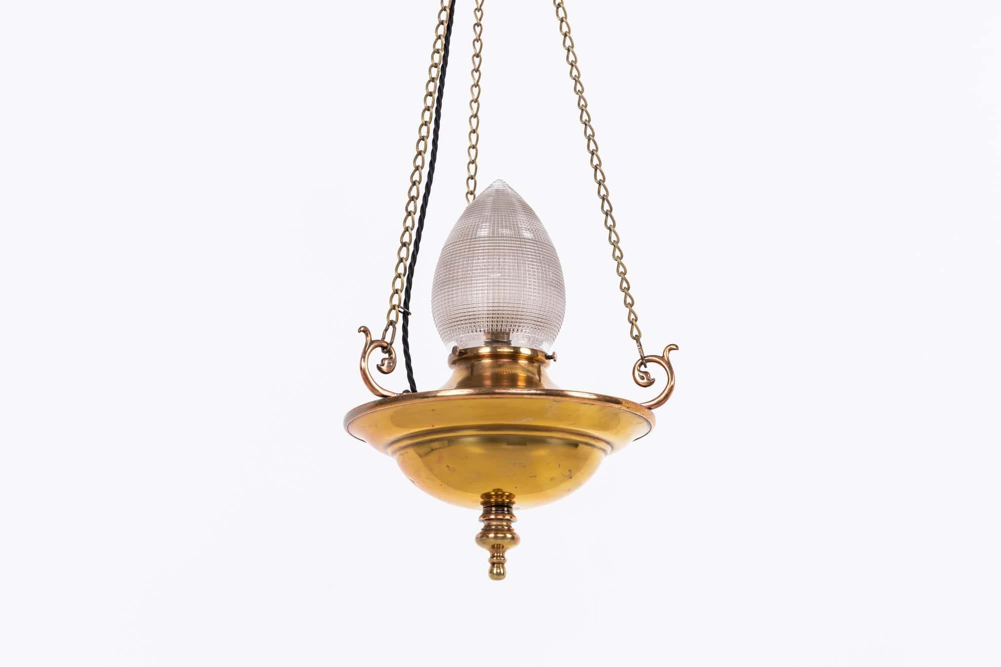 Une lampe de sanctuaire en laiton aux formes élégantes, fabriquée en Angleterre. C.C.

Fabriqué en laiton avec des crochets à volutes en cuivre moulé qui s'est magnifiquement adouci avec le temps. Abat-jour en verre tamponné Holophane en forme de
