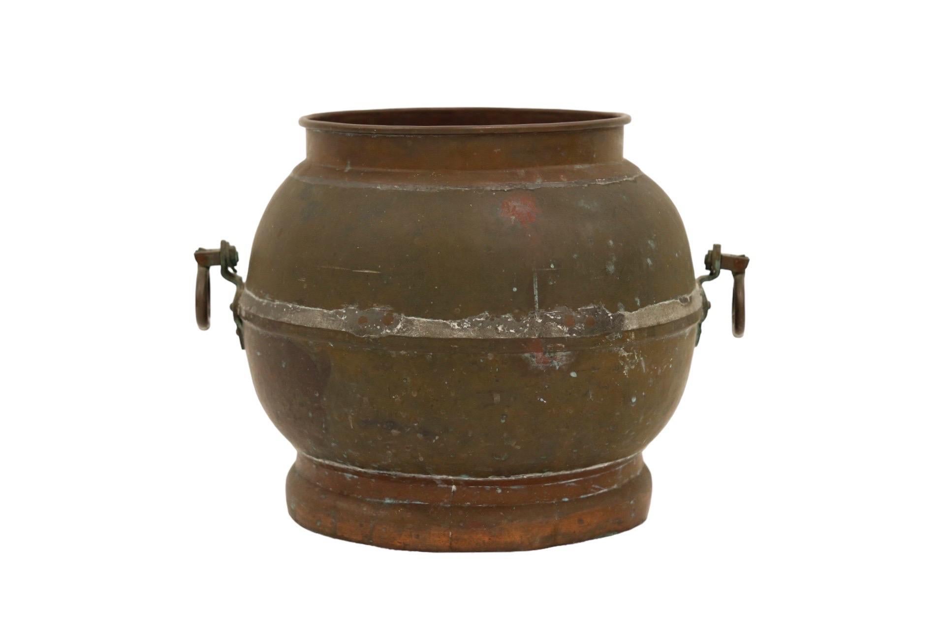 An antique copper planter. Made of two pieces soldered and secured with copper rivets. At each side is an oval drop handle pressed to give the look of a central bead. Finished with a copper lip and foot. Verdigris patina can be seen throughout.
