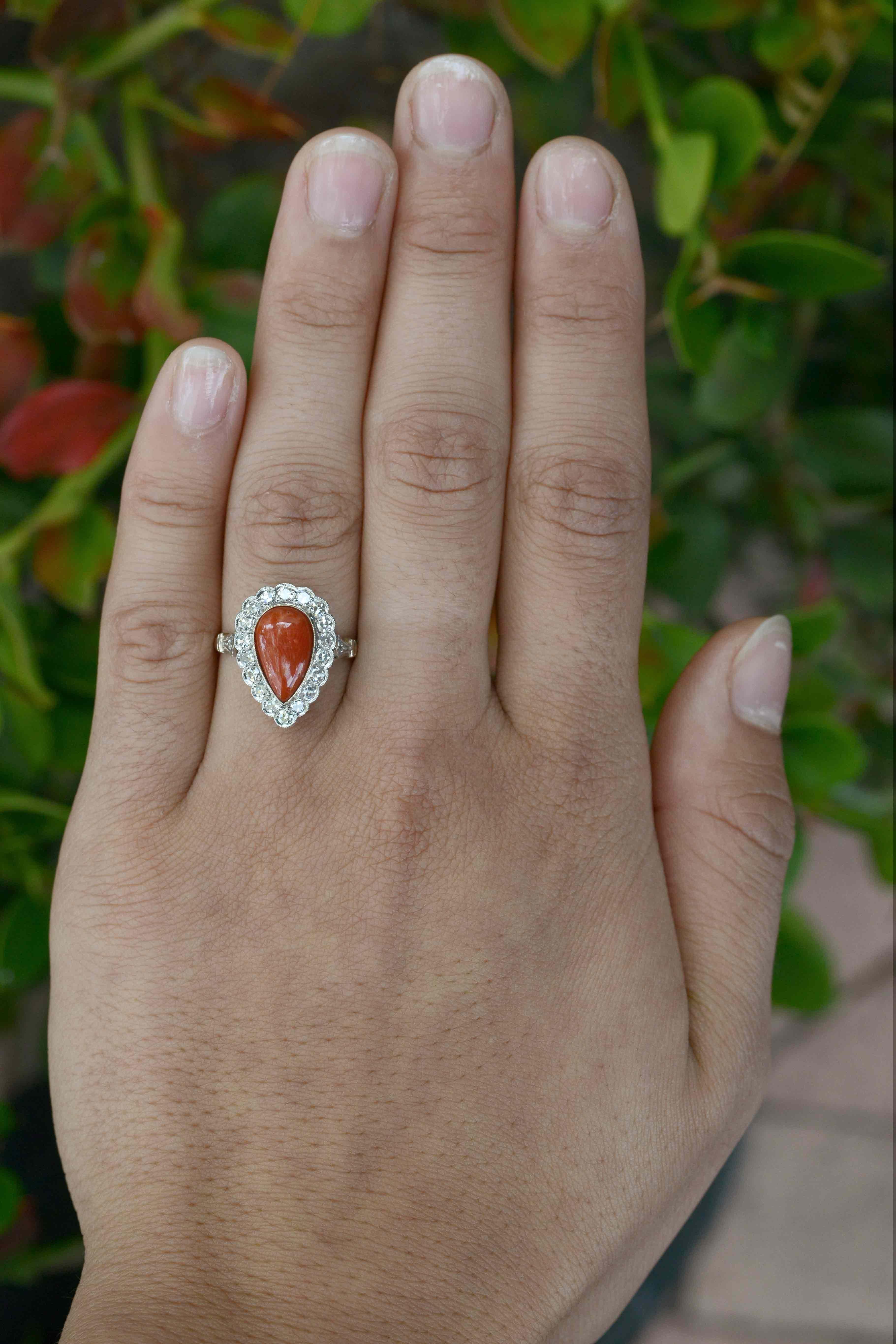 A dramatic red, ox blood coral takes center stage in this authentic antique coral cocktail ring. The pear shaped teardrop, a natural gem from the sea is smartly surrounded by a glittering, 18 diamond halo with scalloped, milgrain details. A dashing