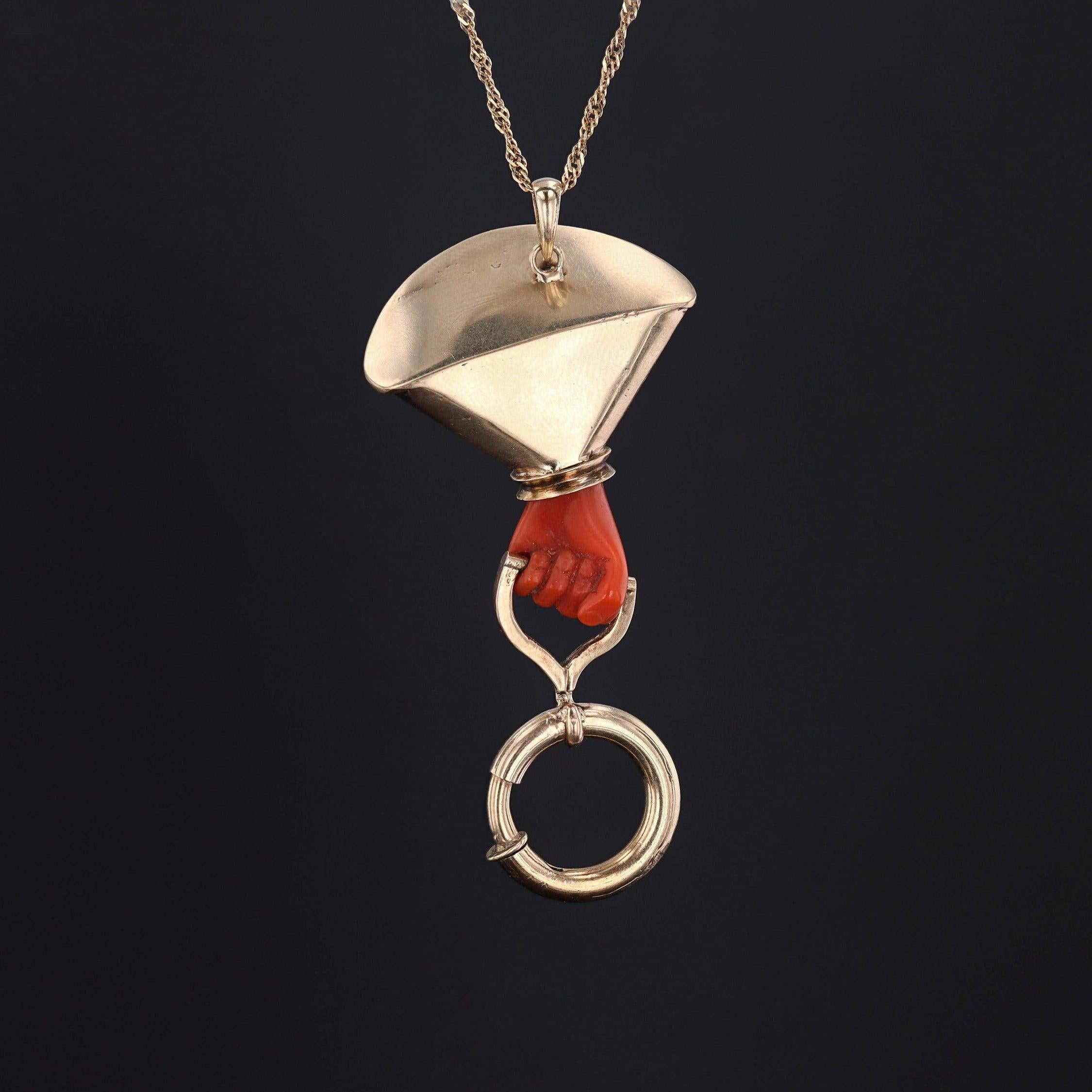 Questo ciondolo in oro 14k è stato convertito da una spilla antica (1870-1890 circa) e presenta una mano di corallo con una molla che stringe un anello a molla con smalto decorativo taille d'epargne sulla manica.

Il pezzo misura 1,4 pollici dalla