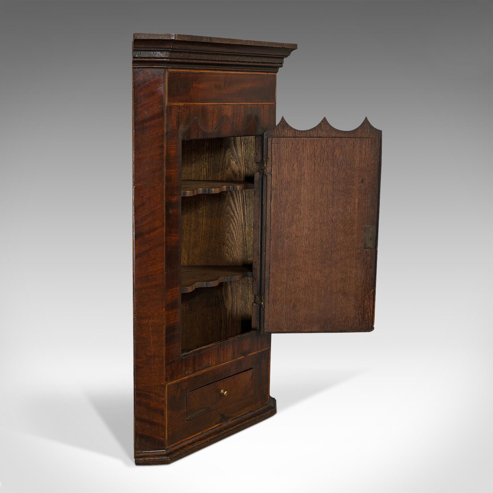 This is an antique corner cabinet. An English, oak and mahogany wall-hanging Georgian cupboard, dating to the late 18th century, circa 1800.

Wonderful Georgian cabinet with delightfully small proportions
Displays a desirable aged patina
Oak and