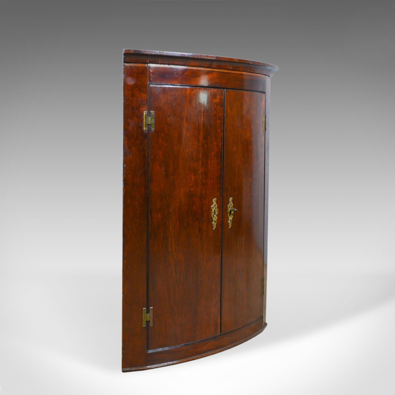 This is an antique corner cabinet. An English, late Georgian, bow fronted, mahogany, hanging corner cupboard dating to the circa 1800.

Deep and rich in color with a desirable aged patina 
Grain interest throughout in the lustrous wax polished