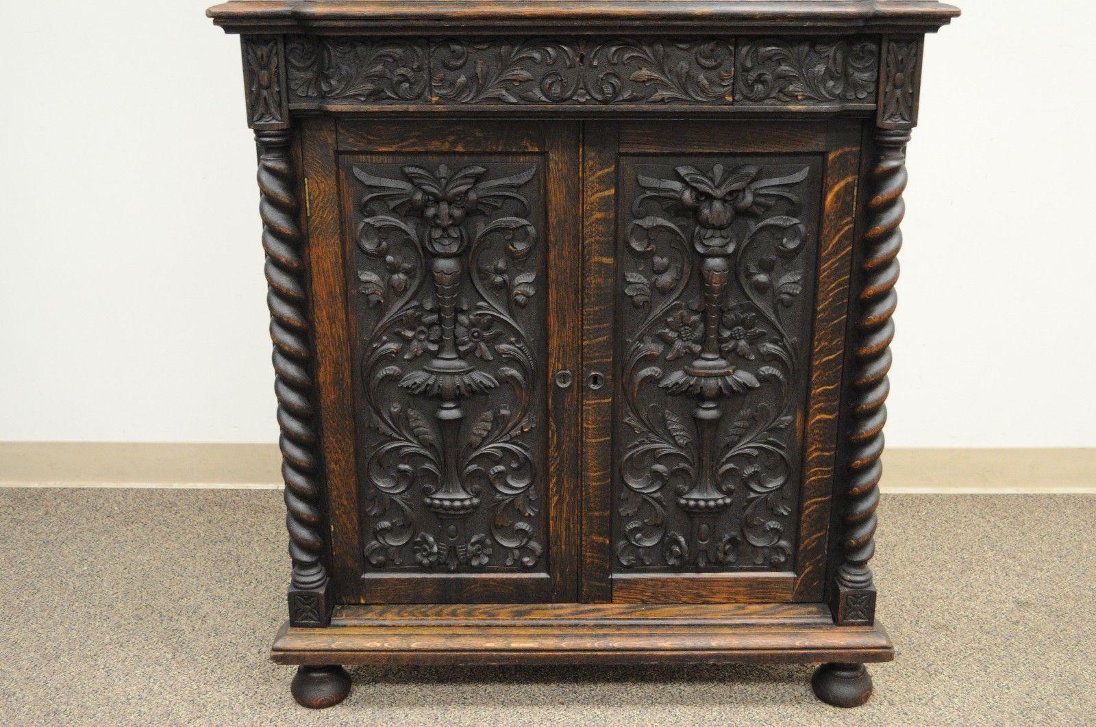 Two part antique renaissance revival carved oak corner china cupboard. Item features two part construction, figural carved oak door fronts with faces, barley twist accents, two adjustable shelves in top and two in bottom, single dovetailed drawer.