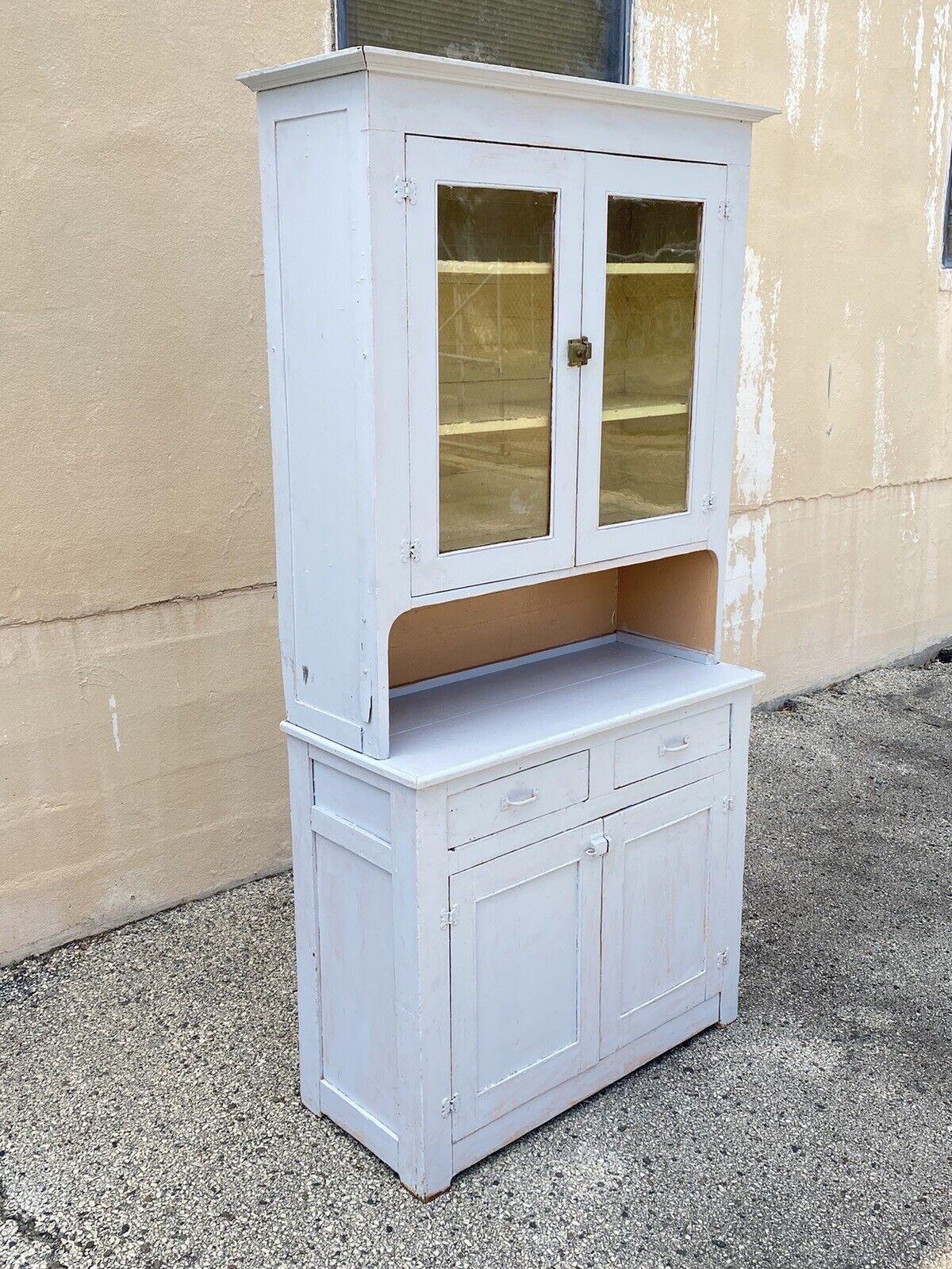 Antique Country Primitive White/Gray Painted 2 Piece Step Back Hutch Kitchen Cupboard. Item features 2 part construction, glass upper doors, 2 drawers, 2 lower cabinet doors, distress painted white/gray finish with peach colored tint, distress