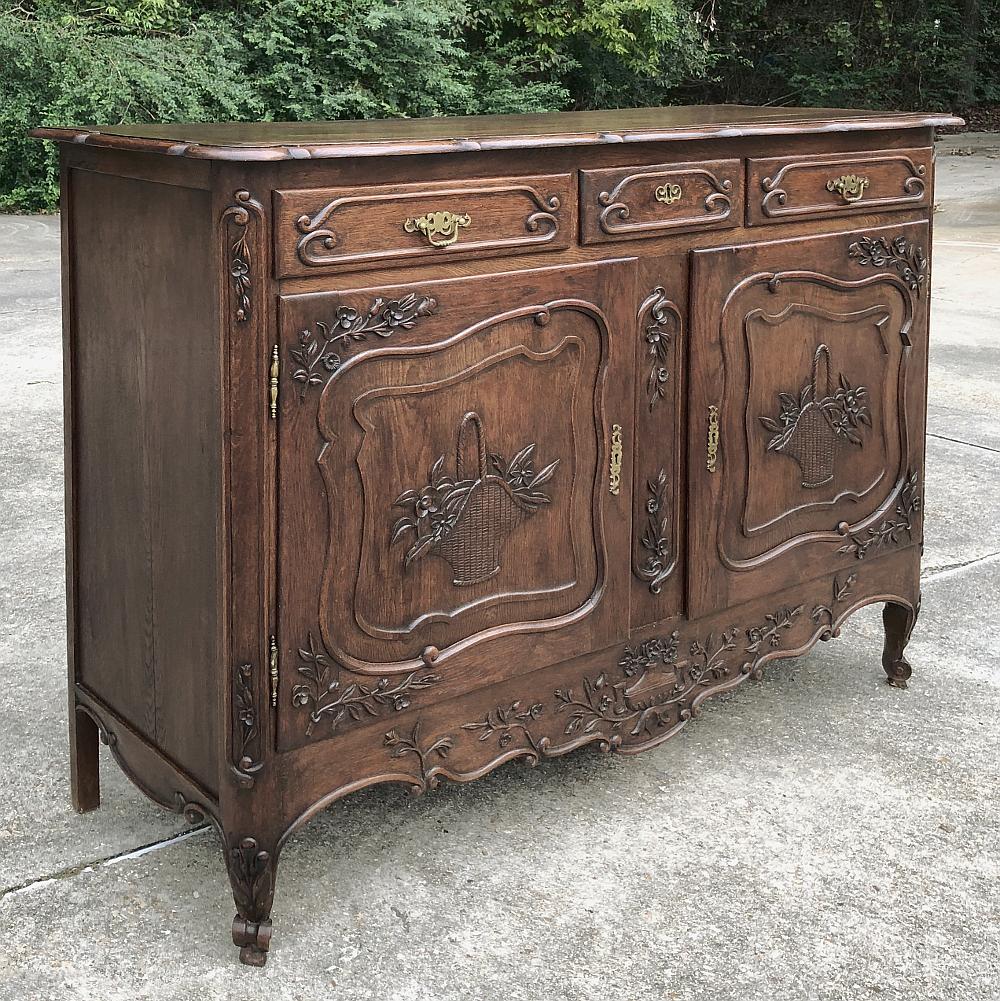 Antique Country French buffet is a very versatile size, combining a lot of storage with three drawers and two cabinets with a piece that's under six feet in width. Baskets of flowers and various wildflowers and foliates are carved across the facade,